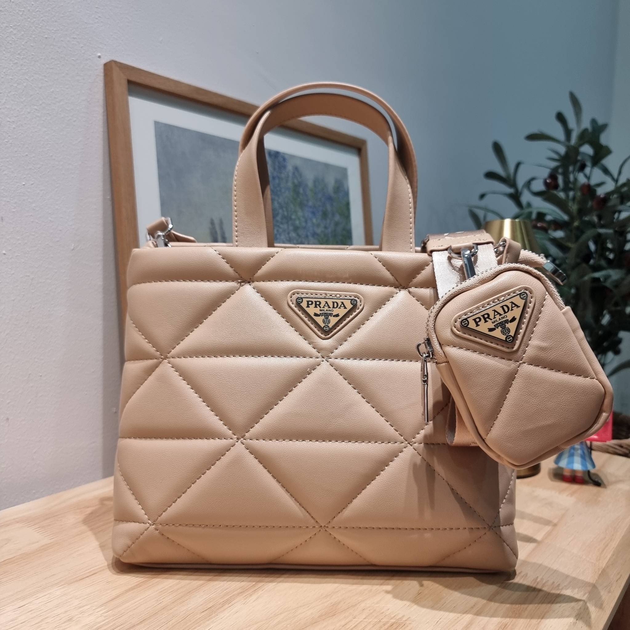 PRADA LEATHER PADDED BAG ใหม่ล่าสุด กับคอลเลคชั่นที่ทำออกมาตอบโจทย์ได้ทุกไลฟ์สไตล์ และเป็นยูนิเซ็กส์ กับกระเป๋าทรงโท้ท ขนาดกำลังดี วัสดุหนังเรียบ ตัดเย็บเดินเส้นลายตาราง ปากกระเป๋ามีซิปเปิดปิด ภายในเป็นช่องโล่ง