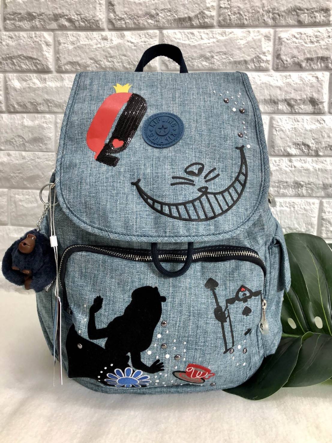 Kipling Disney's Alice in Wonderland Printed Backpack กระเป๋าเป้ Limited คอลเลคชั่น ALICE วัสดุ Denim+Polyester 100% เปิดปิดด้วยฝาปิด กระดุมแม่เหล็ก และซิปรอบ มาพร้อมพวงกุญเเจลิง ถอดเเยกใช้ได้ มีช่องซิปด้านหน้า และด้านหลัง พร้อมช่องใส่ของด้านข้าง 2 ด