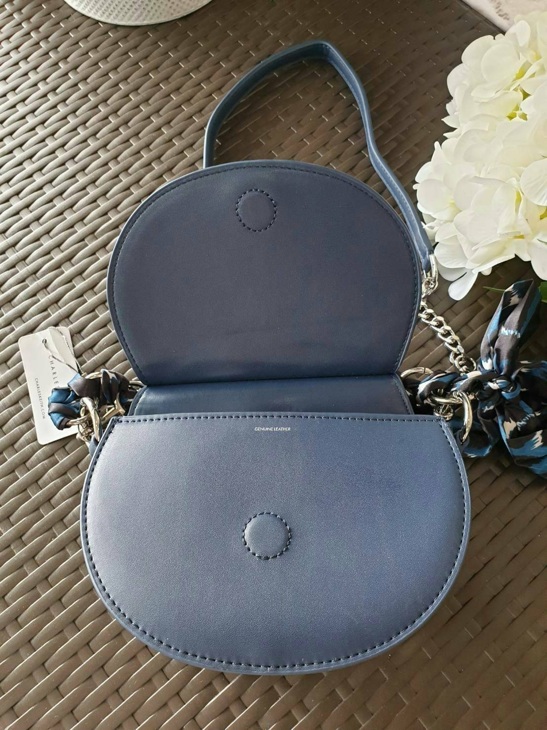 CHARLES & KEITH รุ่น LEATHER SATIN SCARF CROSSBODY BAG SL2-50150828 ราคาปกติช้อป ( ฿3,590.00 ) กระเป๋าถือ และ สะพาย ทรงโค้งมน หนังเรียบ ตั้งอยู่ทรง ด้านหน้าติดโลโก้แบรนด์ อะไหล่เงิน หูจับสายกระเป๋าร้อยเข้ากับห่วงเหล็กกลมๆ ด้วยผ้าลายสวยงามผูกเป็นโบว์เก๋ๆ ถ