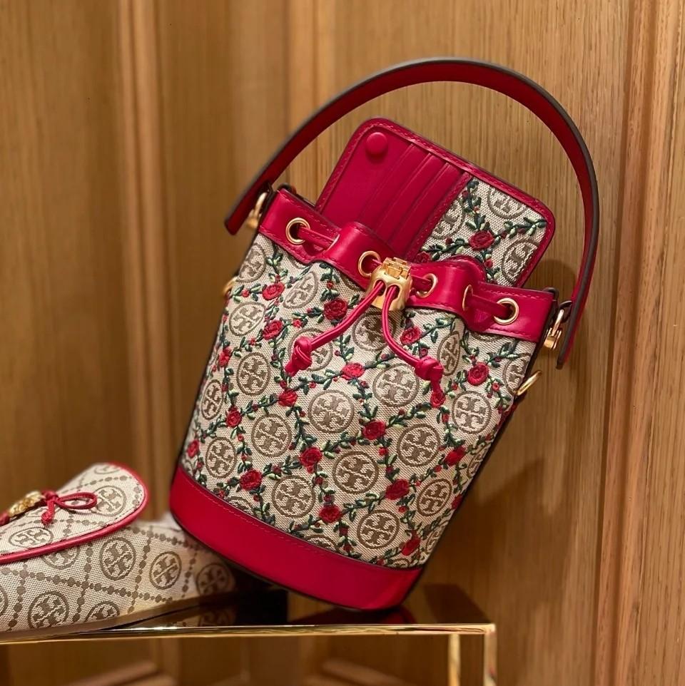 Mini : Tory Burch T Monogram Embroidered Mini Bucket Bag Hazelnut กระเป๋าทรงถังขนาดเล็ก เป็นแพทเทิร์นคลาสสิคที่ได้รับแรงบันดาลใจจากการควิลท์แบบดั้งเดิมของเพนซิลเวเนีย คอลเล็คชั่นบอกเล่าความมีสไตล์เหนือกาลเวลา ลายดอกกุหลาบสีแดงลายปักษ์ วัสดุผ้าสว๊อตซ์วินเท