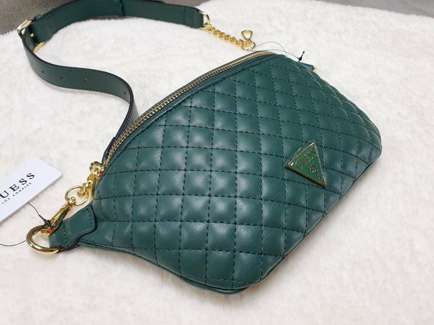 กระเป๋า Guess รุ่นนี้คาดเอว/คาดอก/สะพายข้างได้ครบทุกฟังก์ชั่น ด้านหน้าหนังเป็นลายตาราง ติดโลโก้แบรนด์รูปสามเหลี่ยมด้านหน้า เปิดปิดด้วยซิปยาว ด้านในเป็นช่องกว้างมีช่องซิปด้านใน ตัวกระเป๋าด้านหลังเป็นหนังเรียบ รุ่นนี้มีสายสะพายมา 2 เส้น เส้นแรกเป็นสายหนังปร