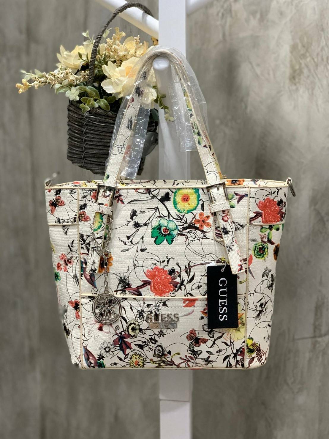 GUESS Women's Medium Floral Tote Bag กระเป๋าถือ คล้องไหล่หรือสะพาย ขนาดกลาง วัสดุหนังpu ลายดอกไม้ชนิดต่างๆรอบใบ เปิดปิดใช้งานด้วยซิปเดียวด้านบน ภายในมีกว้างใส่กระเป๋าสตาวค์ยาว มินิไอแพคได้ หูจับและสายสะพายปรับระดับได้ มาพร้อมกุญแจโลโก้guess สวยน่ารัก