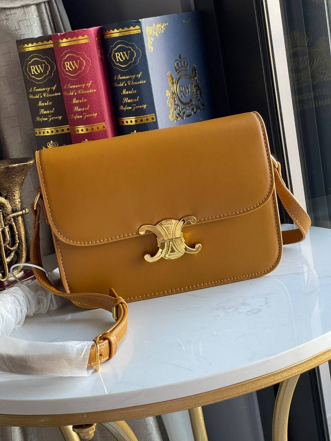 Celine MEDIUM TRIOMPHE BAG IN SHINY มีรูปทรงเป็นกล่องคล้ายกับกระเป๋า Classic Box แต่มีการออกแบบโลโก้ที่สะดุดตาแบบวินเทจ ด้วยดีไซน์ที่ดูโฉบเฉี่ยว แต่คงความคลาสสิคอย่างเต็มเปี่ยม ทำให้เป็นที่ดึงดูดความสนใจของสาวๆ สายสะพายสามารถปรับระดับได้ มีความคล่องตัวในก