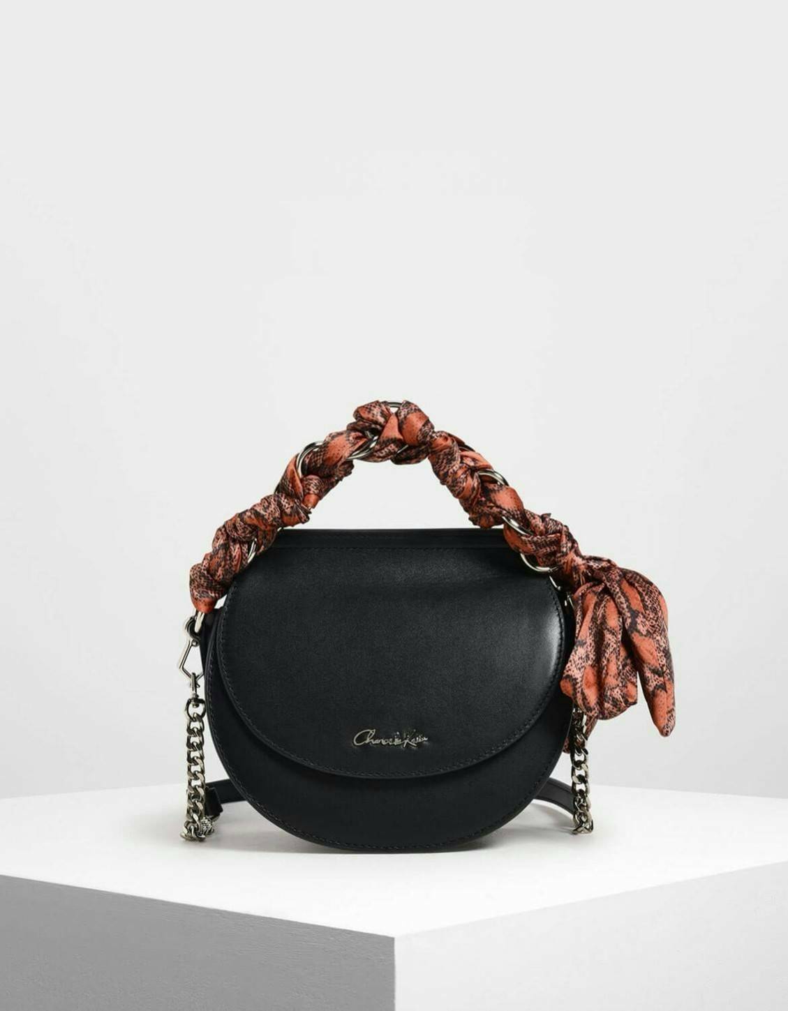 CHARLES & KEITH รุ่น LEATHER SATIN SCARF CROSSBODY BAG SL2-50150828 ราคาปกติช้อป ( ฿3,590.00 ) กระเป๋าถือ และ สะพาย ทรงโค้งมน หนังเรียบ ตั้งอยู่ทรง ด้านหน้าติดโลโก้แบรนด์ อะไหล่เงิน หูจับสายกระเป๋าร้อยเข้ากับห่วงเหล็กกลมๆ ด้วยผ้าลายสวยงามผูกเป็นโบว์เก๋ๆ ถ