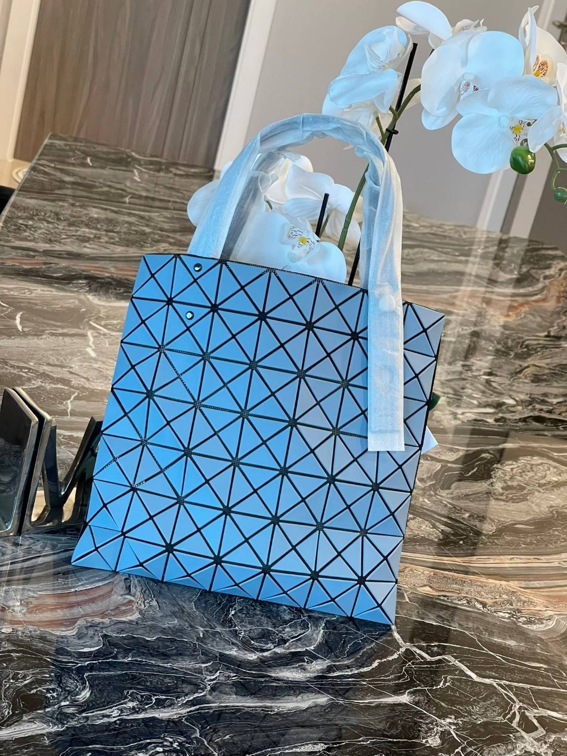 Baobao Issey Miyake Prism Kangaroo tote bag กระเป๋าถือทรงโท้ทที่ประดิษฐ์ขึ้นอย่างเชี่ยวชาญในญี่ปุ่น มาพร้อมแผงเรขาคณิตสำหรับการออกแบบที่ได้รับแรงบันดาลใจจากกระดาษพับ ซิลลูเอทอันเป็นเอกลักษณ์นี้ปิดท้ายด้วยสายรัดแบบอสมมาตร มีการพัฒนาโครงสร้างทรงสามเหลี่ยมเพ
