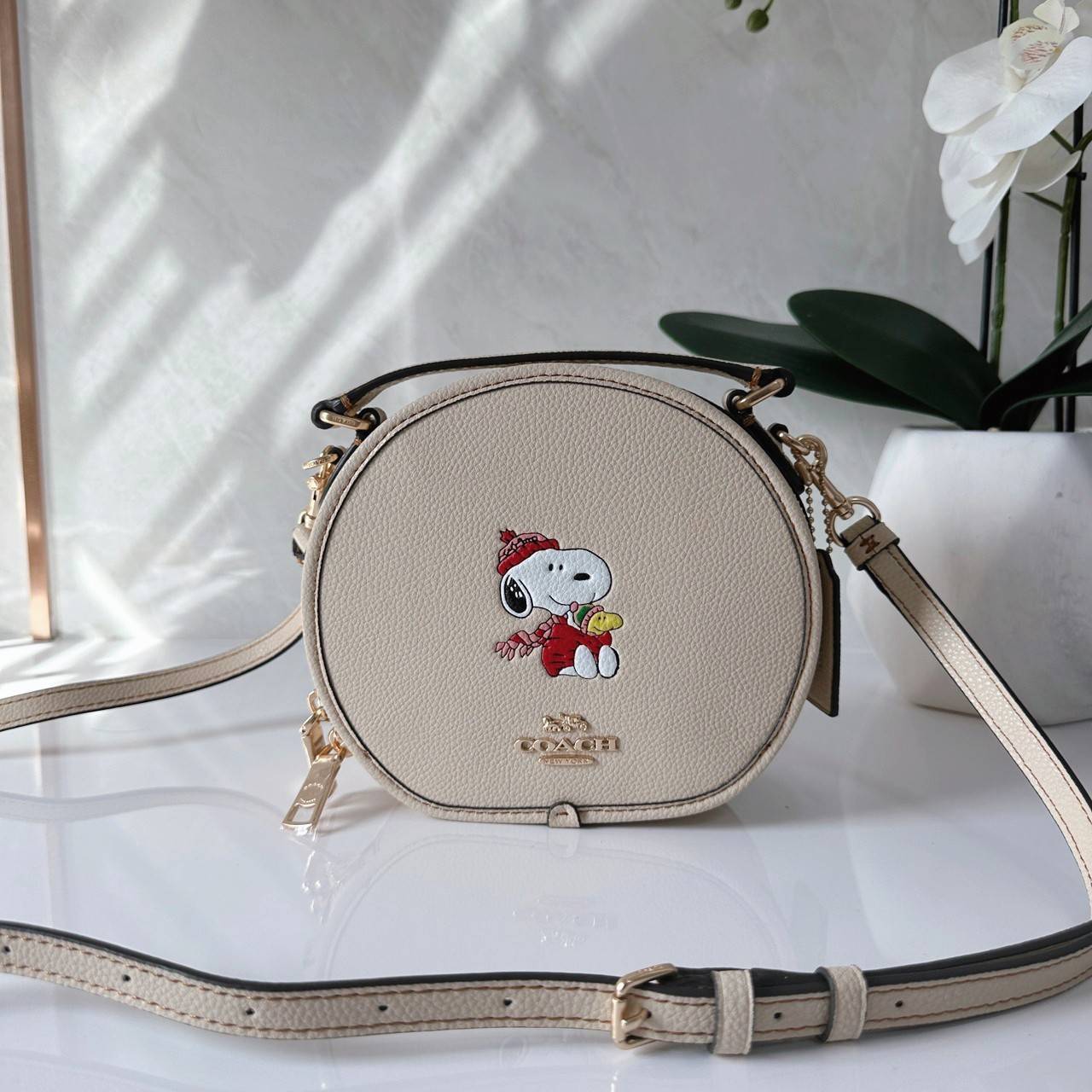 COACH X PEANUTS CANTEEN CROSSBODY WITH SNOOPY PRESENT MOTIF (CE845,CF290) กระเป๋าสะพายข้างทรงกลมไซส์มินิ มีหูจับ วัสหนังแท้ ด้านหน้าโดดเด่นด้วยรูปการ์ตูนSnoopy