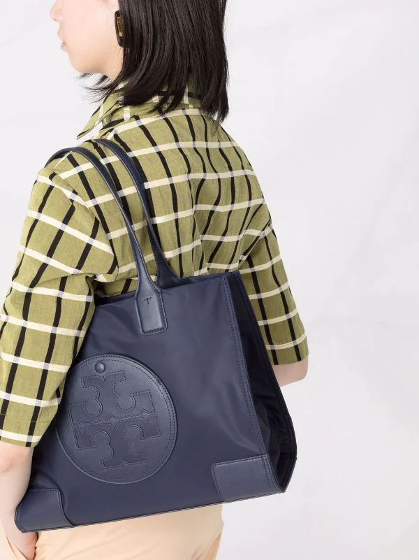 กระเป๋าทรงโท้ทใบใหญ่ TORY BURCH ELLA TOTE BAG วัสดุ NYLON ทั้งใบตัดด้วยหนังสีดำ แต่งโลโก้แบรนด์ด้านหน้า ด้านข้างมีกระดุม สามารถขยายทรงได้ ด้านในเปิดปิดด้วยกระดุมแม่เหล็กฝัง ช่องกว้างหลักหนึ่งช่องและช่องซิปอีกช่อง สามารถใส่แล็ปท็อปได้สบาย ใบใหญ่เว่อวัง ไอเ