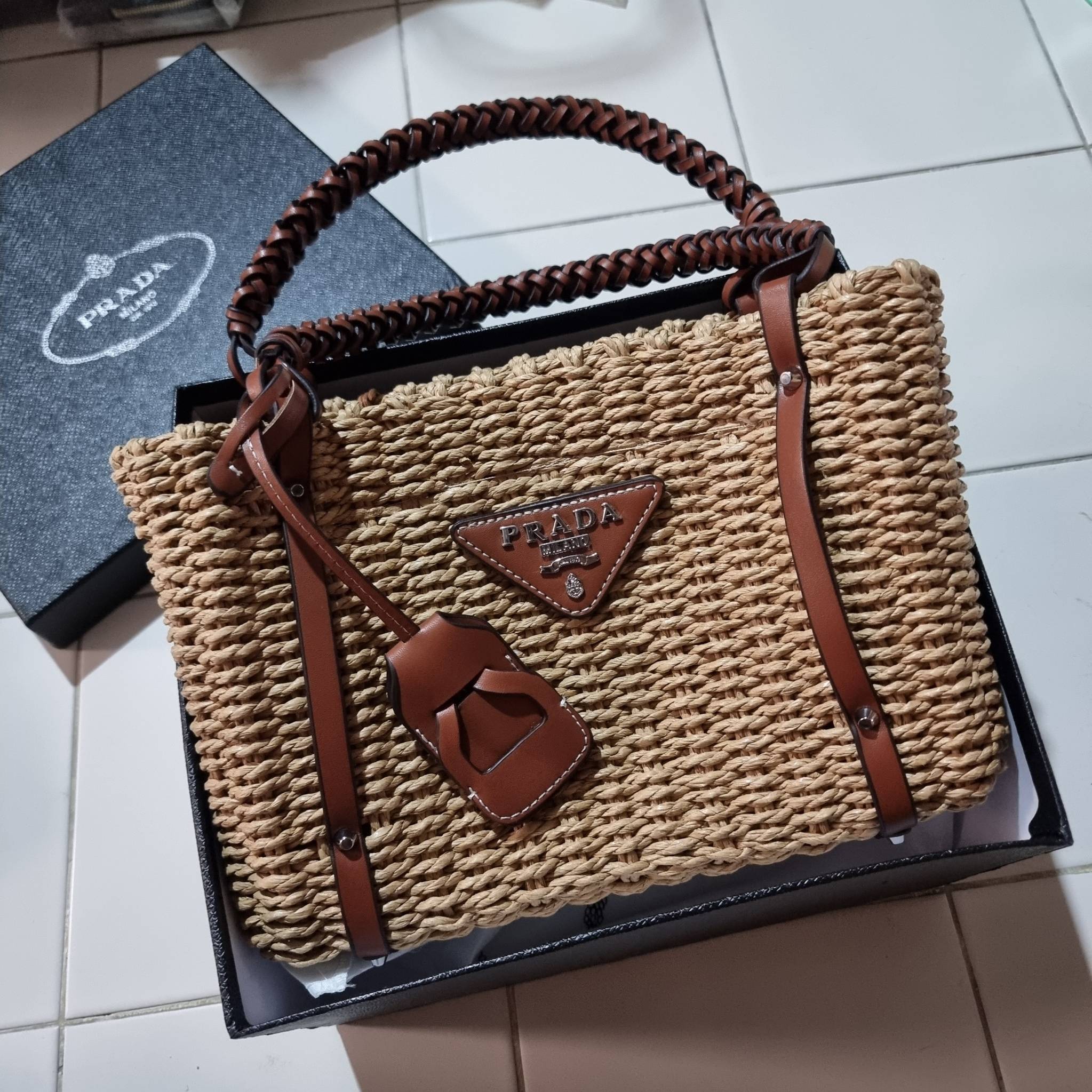 PRADA CORN HUSK AND LEATHER TOTE ธรรมชาติเป็นหนึ่ง!! กับอีกไอเท็มรักษ์โลก ด้วยดีไซน์ล้ำทันสมัย ผสานกับวัสดุจากธรรมชาติ ออกมาเป็นลายสานที่สวยหรู ไม่กระด้าง กระเป๋าทรงโท้ท ขนาดกำลังสวย มาพร้อมหูจับในตัว มีซิปรูปเปิด-ปิดที่ปากกระเป๋า ภายในโล่งกว้าง ใส่ของได้