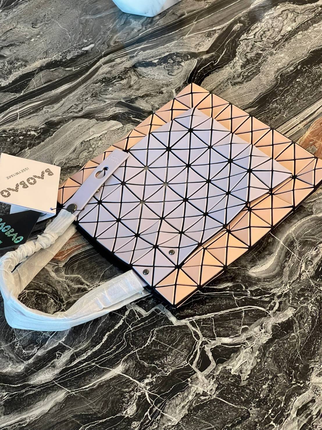 Baobao Issey Miyake Prism Kangaroo tote bag กระเป๋าถือทรงโท้ทที่ประดิษฐ์ขึ้นอย่างเชี่ยวชาญในญี่ปุ่น มาพร้อมแผงเรขาคณิตสำหรับการออกแบบที่ได้รับแรงบันดาลใจจากกระดาษพับ ซิลลูเอทอันเป็นเอกลักษณ์นี้ปิดท้ายด้วยสายรัดแบบอสมมาตร มีการพัฒนาโครงสร้างทรงสามเหลี่ยมเพ