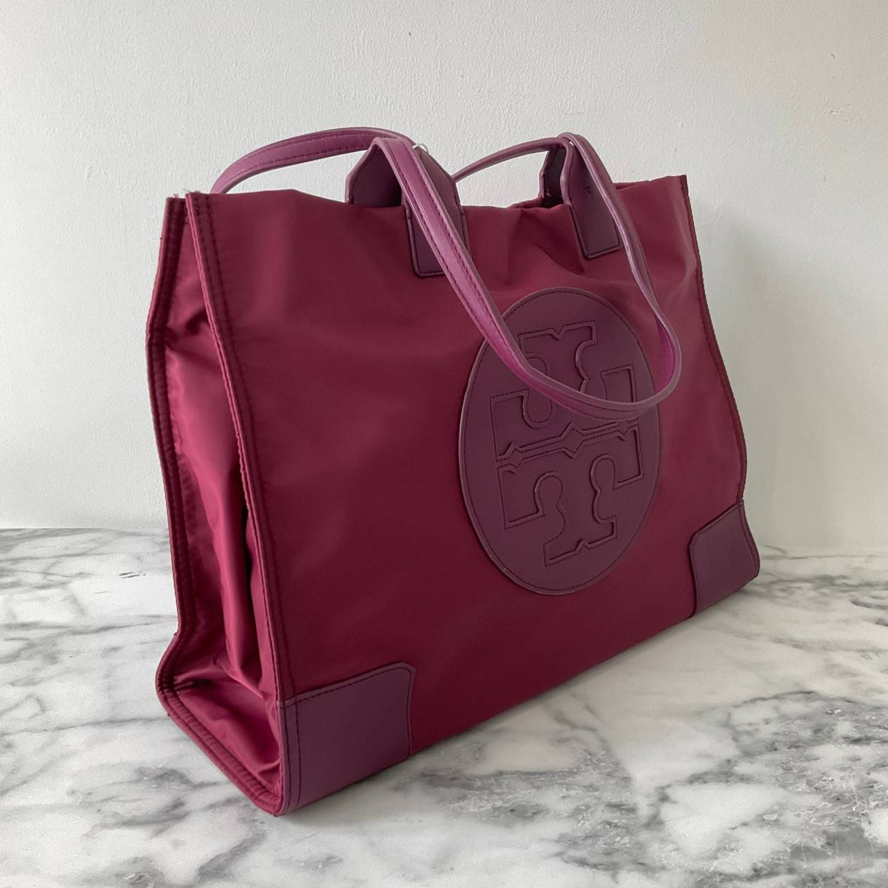 กระเป๋าทรงโท้ทใบใหญ่ TORY BURCH ELLA TOTE BAG วัสดุ NYLON ทั้งใบตัดด้วยหนังสีดำ แต่งโลโก้แบรนด์ด้านหน้า ด้านข้างมีกระดุม สามารถขยายทรงได้ ด้านในเปิดปิดด้วยกระดุมแม่เหล็กฝัง ช่องกว้างหลักหนึ่งช่องและช่องซิปอีกช่อง สามารถใส่แล็ปท็อปได้สบาย ใบใหญ่เว่อวัง ไอเ