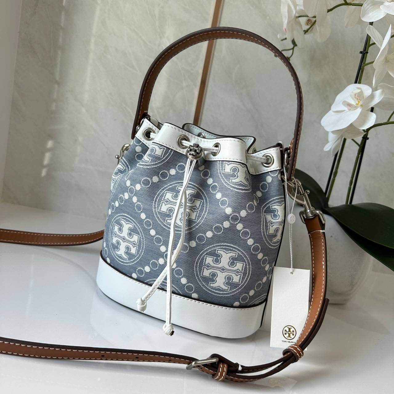 TORY BURCH T Monogram Denim Bucket Bag MEDIUM คอลเลคชั่นใหม่ รูปแบบคลาสสิค พกพาความหรูหราไปได้ทุกที่ด้วยกระเป๋าทรง Bucket ขนาดกลางและปิดด้วยเชือกรูดพร้อมโลโก้แวววาว วัสดุผ้าเดนิมแจ็คการ์ด ตัดขอบหนังแท้