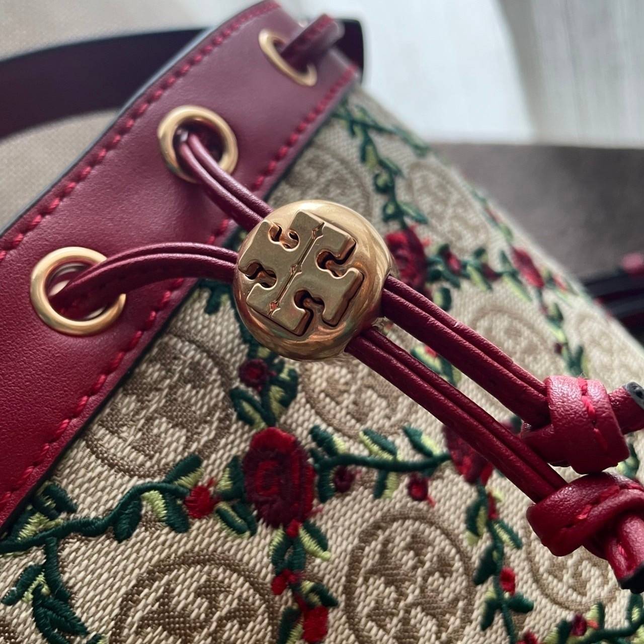 Mini : Tory Burch T Monogram Embroidered Mini Bucket Bag Hazelnut กระเป๋าทรงถังขนาดเล็ก เป็นแพทเทิร์นคลาสสิคที่ได้รับแรงบันดาลใจจากการควิลท์แบบดั้งเดิมของเพนซิลเวเนีย คอลเล็คชั่นบอกเล่าความมีสไตล์เหนือกาลเวลา ลายดอกกุหลาบสีแดงลายปักษ์ วัสดุผ้าสว๊อตซ์วินเท