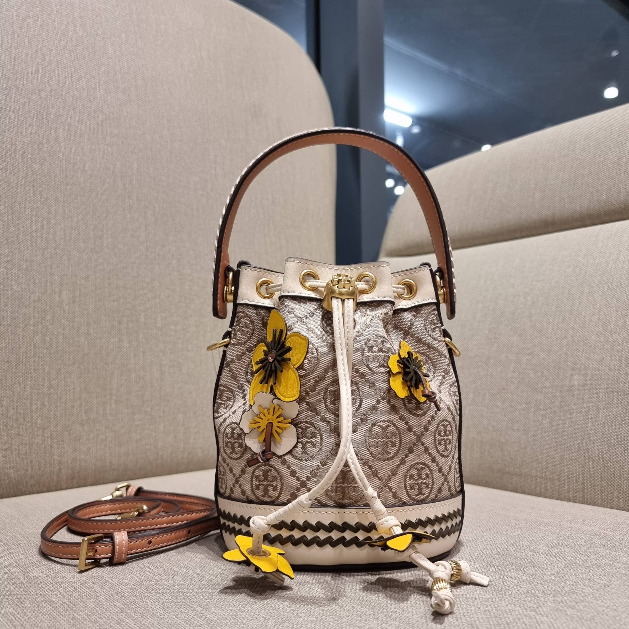 TORY BURCH MINI T MONOGRAM FLORAL BUCKET BAG คอลเลคชั่นใหม่ พร้อมเสิร์ฟความสวยให้ถึงบ้าน!! กระเป๋าบัคเก็ตทรงยอดนิยม ไซส์มินิ ดีไซน์ใหม่ล่าสุด สไตล์งานคราฟ มีลูกเล่นประดับดอกไม้กับตัวกระเป๋า และตัวรูดสาย วัสดุผ้า jacquard ตัดสลับหนังแท้ หูจับและขอบกระเป๋าต