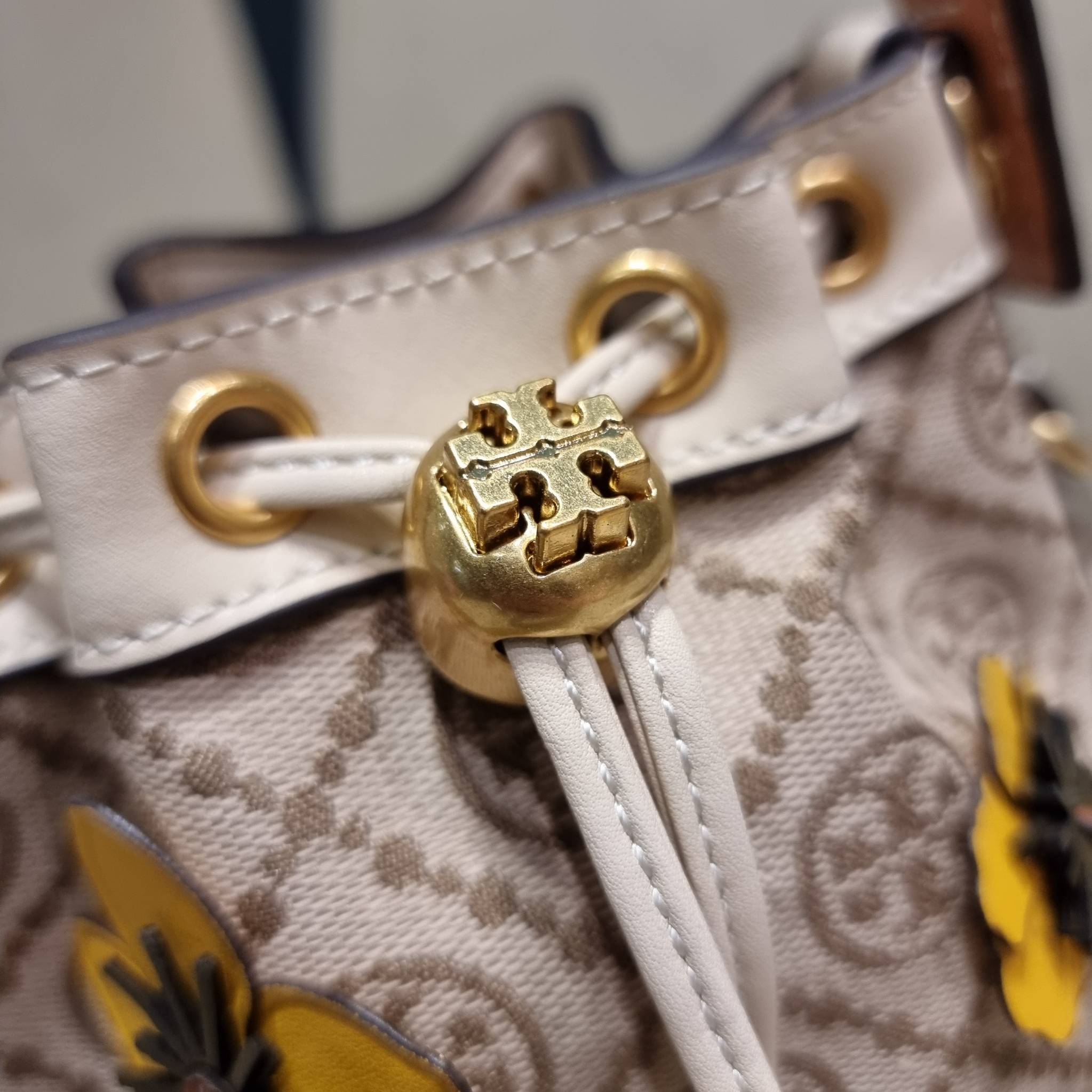 TORY BURCH MINI T MONOGRAM FLORAL BUCKET BAG คอลเลคชั่นใหม่ พร้อมเสิร์ฟความสวยให้ถึงบ้าน!! กระเป๋าบัคเก็ตทรงยอดนิยม ไซส์มินิ ดีไซน์ใหม่ล่าสุด สไตล์งานคราฟ มีลูกเล่นประดับดอกไม้กับตัวกระเป๋า และตัวรูดสาย วัสดุผ้า jacquard ตัดสลับหนังแท้ หูจับและขอบกระเป๋าต