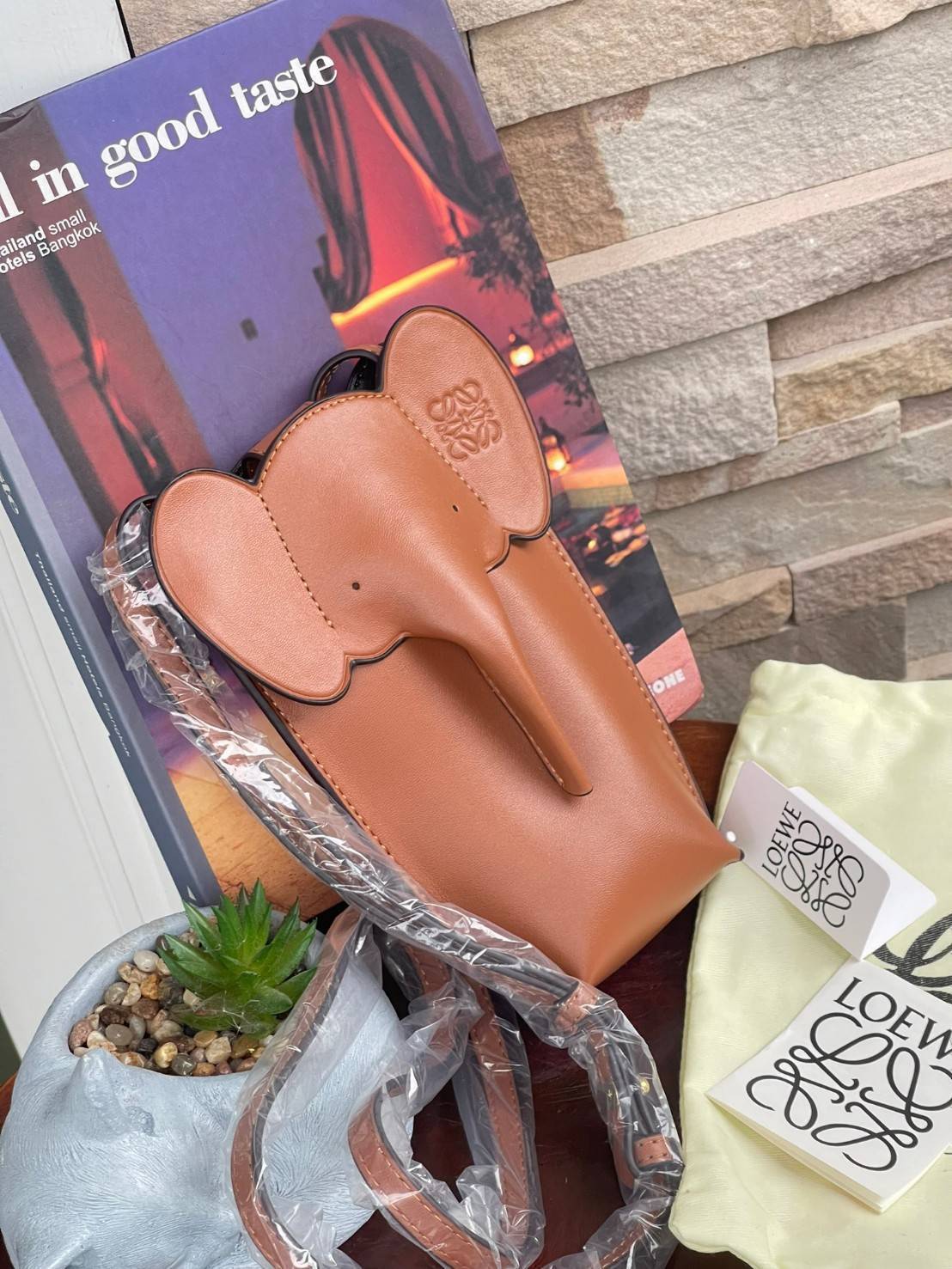 Loewe Leather Elephant Phone Holder แบรนด์หรูจากประเทศสเปนอย่าง โลเอเว่ (LOEWE) หลายๆคนคงนึกถึงกระเป๋ารูปทรงช้างขนาดเล็ก ที่เป็นเหมือนหนึ่งในซิกเนเจอร์ของแบรนด์ มีทั้งแบบสะพายข้าง แบบถือ รวมไปถึงในแบบเครื่องหนังชิ้นเล็กอย่างกระเป๋าใส่มือถือรุ่นนี้ ผลิตจาก