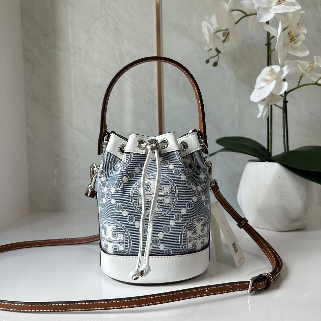TORY BURCH Mini T Monogram Denim Bucket Bag คอลเลคชั่นใหม่ รูปแบบคลาสสิค พกพาความหรูหราไปได้ทุกที่ด้วยกระเป๋าทรง Bucket ขนาดกลางและปิดด้วยเชือกรูดพร้อมโลโก้แวววาว วัสดุผ้าเดนิมแจ็คการ์ด ตัดขอบหนังแท้ สวยหรู ทันสมัยสุดๆคะ