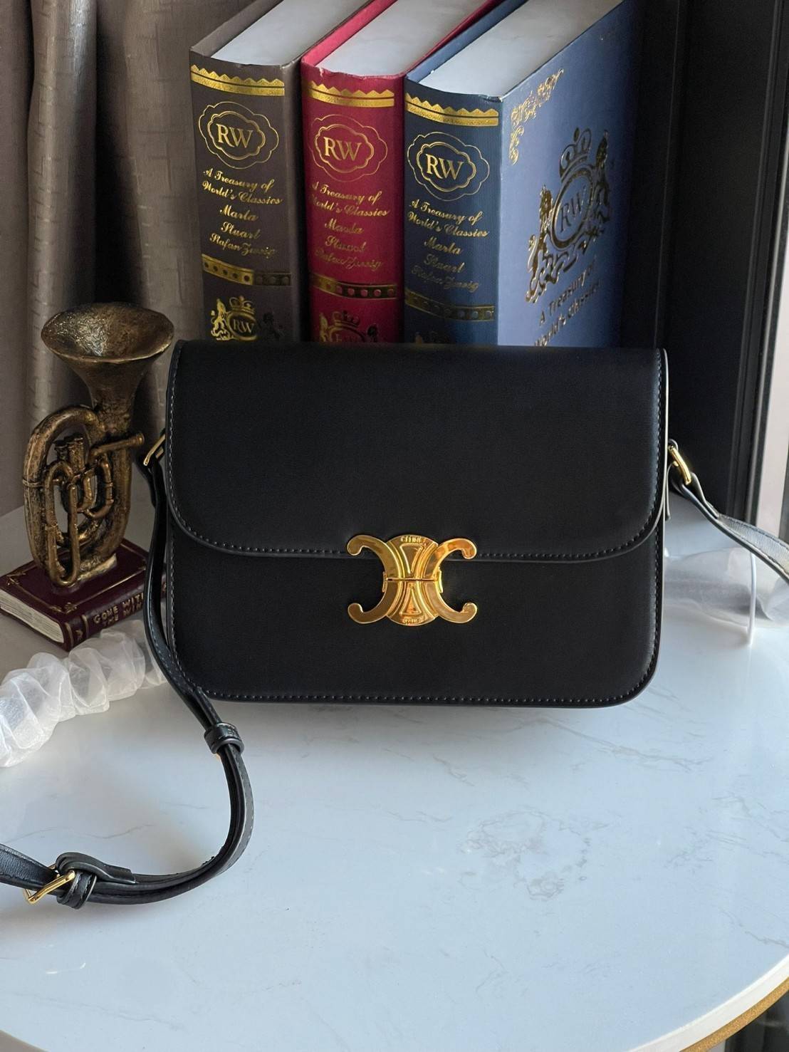 Celine MEDIUM TRIOMPHE BAG IN SHINY มีรูปทรงเป็นกล่องคล้ายกับกระเป๋า Classic Box แต่มีการออกแบบโลโก้ที่สะดุดตาแบบวินเทจ ด้วยดีไซน์ที่ดูโฉบเฉี่ยว แต่คงความคลาสสิคอย่างเต็มเปี่ยม ทำให้เป็นที่ดึงดูดความสนใจของสาวๆ สายสะพายสามารถปรับระดับได้ มีความคล่องตัวในก