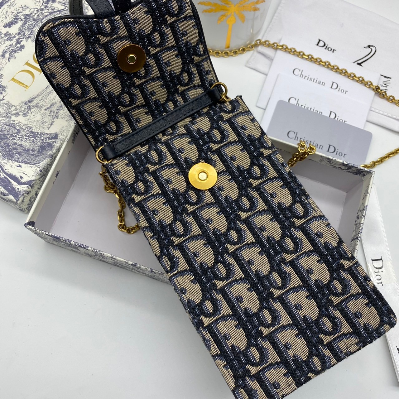 หนังแท้ DIOR PHONE BAG / DIOR PHONE HOLDER BAG กระเป๋าใส่โทรศัพท์เอกลักษณ์ของความหรู สายสะพายโซ่อะไหล่ทอง วัสดุหนังแท้และผ้า Jacquard อย่างดีสวยงามที่สุด ผสมผสานความสง่างามและคลาสสิกที่เข้ากับยุคสมัย ด้านหน้าโดดเด่นด้วยซิกเนเจอร์แบรนด์ เป็นอีกหนึ่งรุ่นที่
