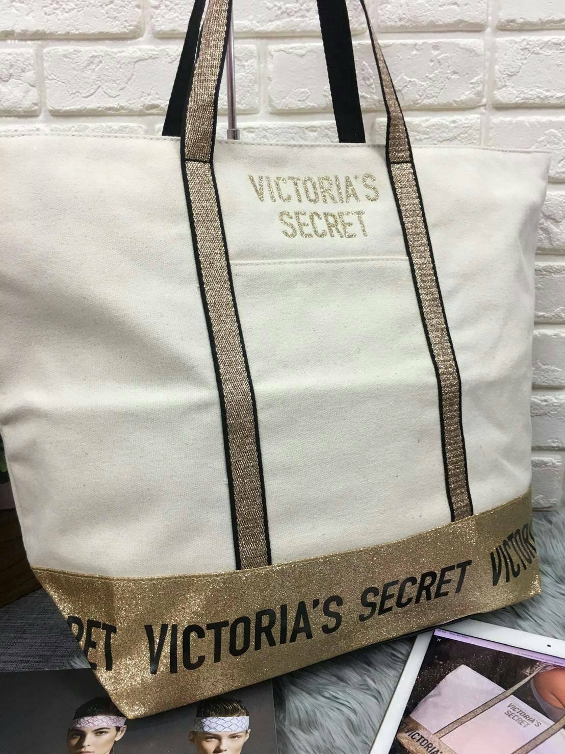Victoria's Secret Canvas Tote Bag กระเป๋าสะพายวัสดุแคสวาสสีครีม ด้านล่างเป็นกลิตเตอร์ สกรีนชื่อแบรนด์ ฐานกระเป๋าเป็นหนัง ด้านหน้ามีช่องเล็กไว้ใส่ของได้ เปิดปิดด้วยซิป ซับในลายแบรนด์ มีช่องซิปเล็กแยกใส่ของ1ช่อง จุของได้เยอะมาก