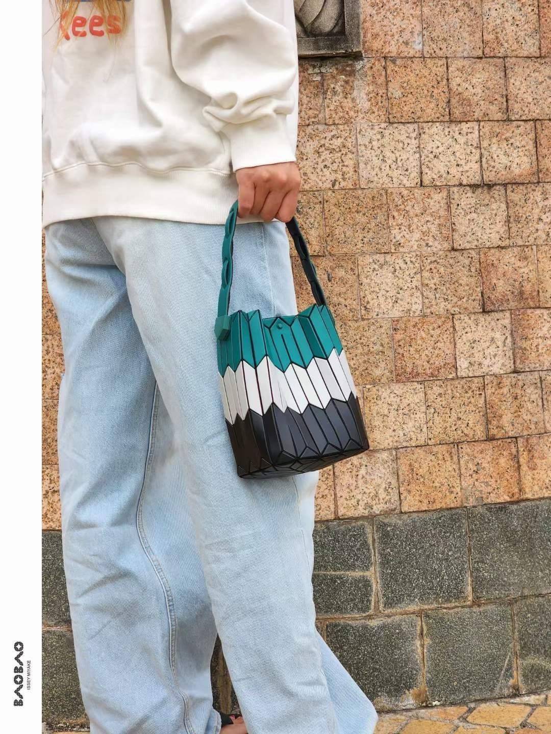 Small : BAO BAO ISSEY MIYAKE SMALL BUCKET เป็นกระเป๋าบัคเก็ตขนาดเล็กสามารถใช้ใส่กระเป๋าสตางค์และโทรศัพท์มือถือได้ ซีรีย์ใหม่นี้มีจุดเด่นที่แผ่นรูปทรงสี่เหลี่ยมด้านขนานในแนวตั้ง เกิดเป็นรูปทรงสามมิติซึ่งแตกต่างไปจากรูปทรงที่เกิดขึ้นจากแผ่นสามเหลี่ยม หูหิ้ว