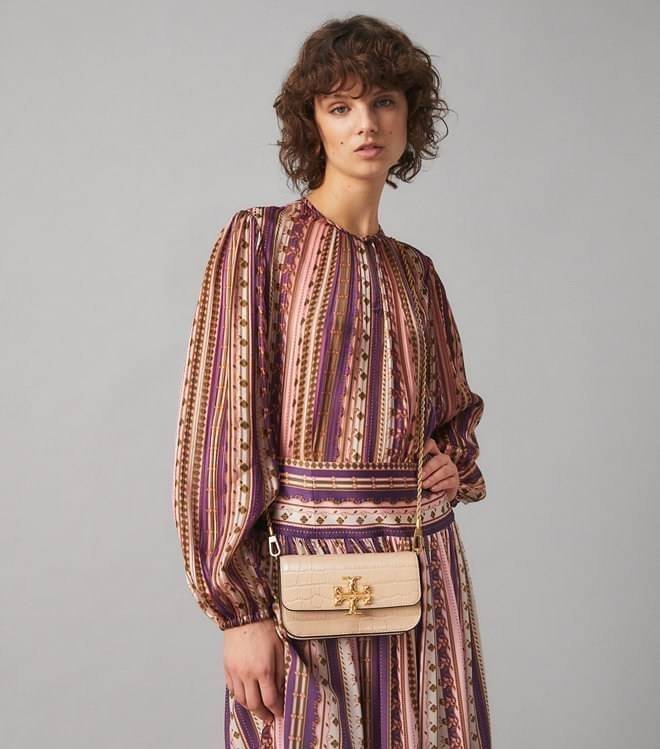 Tory Burch Eleanor Crocodile-Embossed Phone Crossbody Bag จุดเด่นของรุ่นนี้คือดีไซน์ออกมาในสไตล์คลาสสิกที่มาพร้อมกับฮาร์ดแวร์ที่ทำจากวัสดุทองเหลืองและสายสะพายโซ่เกลียวสีทอง ซึ่งการออกแบบได้รับแรงบันดาลใจมาจากเครื่องประดับ รูปทรงกะทัดรัดจึงสามารถสะพายใช้งา