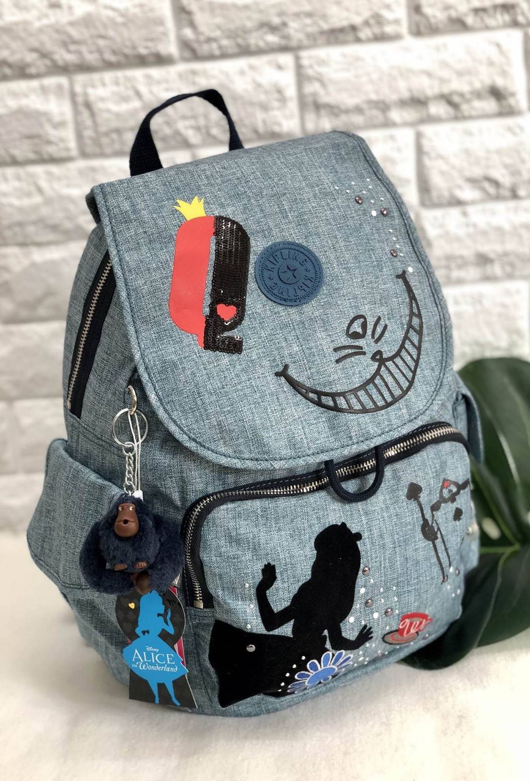 Kipling Disney's Alice in Wonderland Printed Backpack กระเป๋าเป้ Limited คอลเลคชั่น ALICE วัสดุ Denim+Polyester 100% เปิดปิดด้วยฝาปิด กระดุมแม่เหล็ก และซิปรอบ มาพร้อมพวงกุญเเจลิง ถอดเเยกใช้ได้ มีช่องซิปด้านหน้า และด้านหลัง พร้อมช่องใส่ของด้านข้าง 2 ด