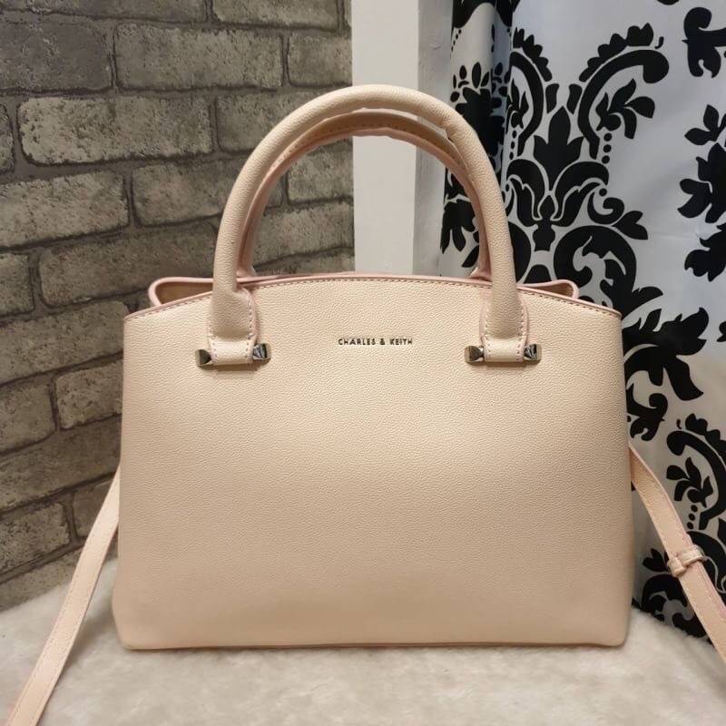 CHARLES & KEITH CLASSIC TOP HANDLE BAG กระเป๋าถือหรือสะพายใบใหญ่ ทรงแข็ง หนัง pu สวย ดีไซน์เรียบหรู ดูดี ด้านหน้าป้ายโลโก้แบบนูน ด้านหลังมีซ่องซิป 1 ช่อง เปิด-ปิดแบบกระดุมแม่เหล็ก ภายในมี 2 ช่องใหญ่ คั่นกลางด้วยช่องซิป มีหมุดรองรองฐานสี่มุม มาพร้อมสายสะพา