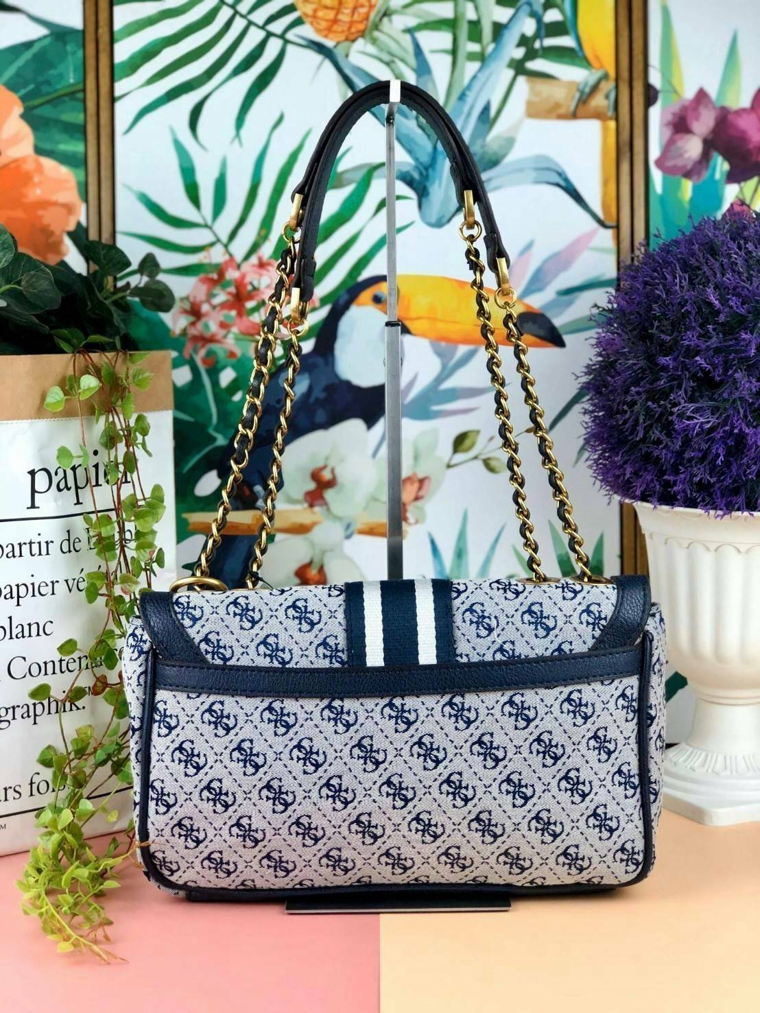 Guess Logo city handbag กระเป๋าสะพายไหล่ ตัวกระเป๋าเป็นผ้าลาย signature ของแบรนด์ ตัดกับหนังที่ตัวขอบกระเป๋า มาพร้อมพวงกุญแจโลโก้แบรนด์ ด้านหน้ามีโลโก้แบรนด์ ด้านหลังมีช่องใส่โทรศัพท์/บัตรได้ เปิดปิดแบบกระดุมแม่เหล็กซ้าย-ขวา ด้านในมีช่องซิป เล็ก 1 ช่อง แล