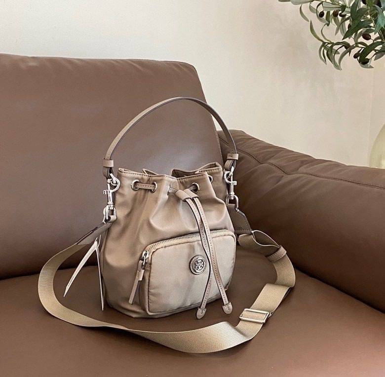 Tory Burch Virginia Nylon Bucket Bag / Tory Burch logo-plaque bucket bag กระเป๋าสะพายทรงบัคเก็ต เปิด-ปิดหนังรูดปากกระเป๋า มีหูหิ้วในตัว คล้องแขนเก๋ๆ ภายในเป็นช่องโล่ง มีช่องย่อย ใส่ของสำคัญจุกจิกได้ มีสายครอส จะสะพายไปไหนก็ได้ทุกโอกาส สวยเลิศทุกสี พร้อมส่