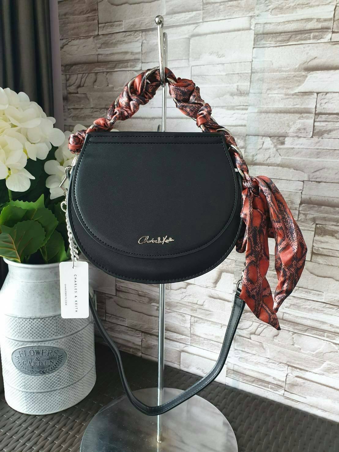 CHARLES & KEITH รุ่น LEATHER SATIN SCARF CROSSBODY BAG SL2-50150828 ราคาปกติช้อป ( ฿3,590.00 ) กระเป๋าถือ และ สะพาย ทรงโค้งมน หนังเรียบ ตั้งอยู่ทรง ด้านหน้าติดโลโก้แบรนด์ อะไหล่เงิน หูจับสายกระเป๋าร้อยเข้ากับห่วงเหล็กกลมๆ ด้วยผ้าลายสวยงามผูกเป็นโบว์เก๋ๆ ถ
