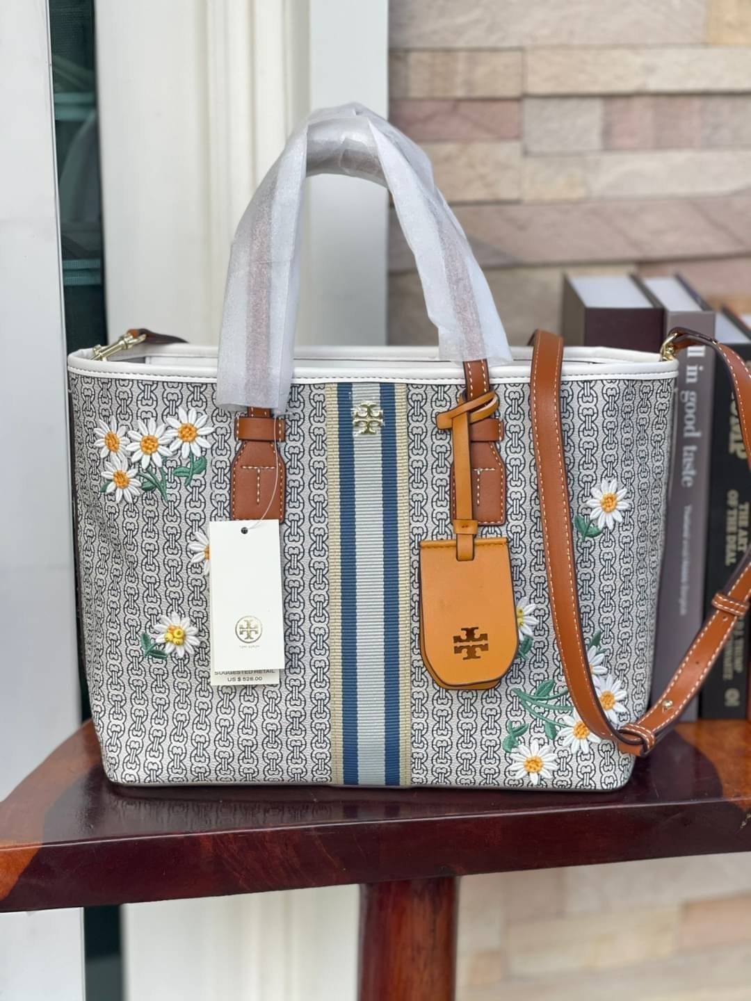Tory burch Gemini Canvas Applique Small Tote Bag กระเป๋าสุดปังจากทอรี่ เบริช์(Tory Burch) อย่างเจมิไนลิงค์ ในทรง tote bag มีเอกลักษณ์โดดเด่นที่ลายทางตรงกลาง มีการพิมพ์แพทเทิรน์โซ่แบบเรียบหรู เพิ่มความน่ารักจากดอกเดรซี่ที่ถูกจัดวางให้ดูมีสีสัน มีสายสะพายให