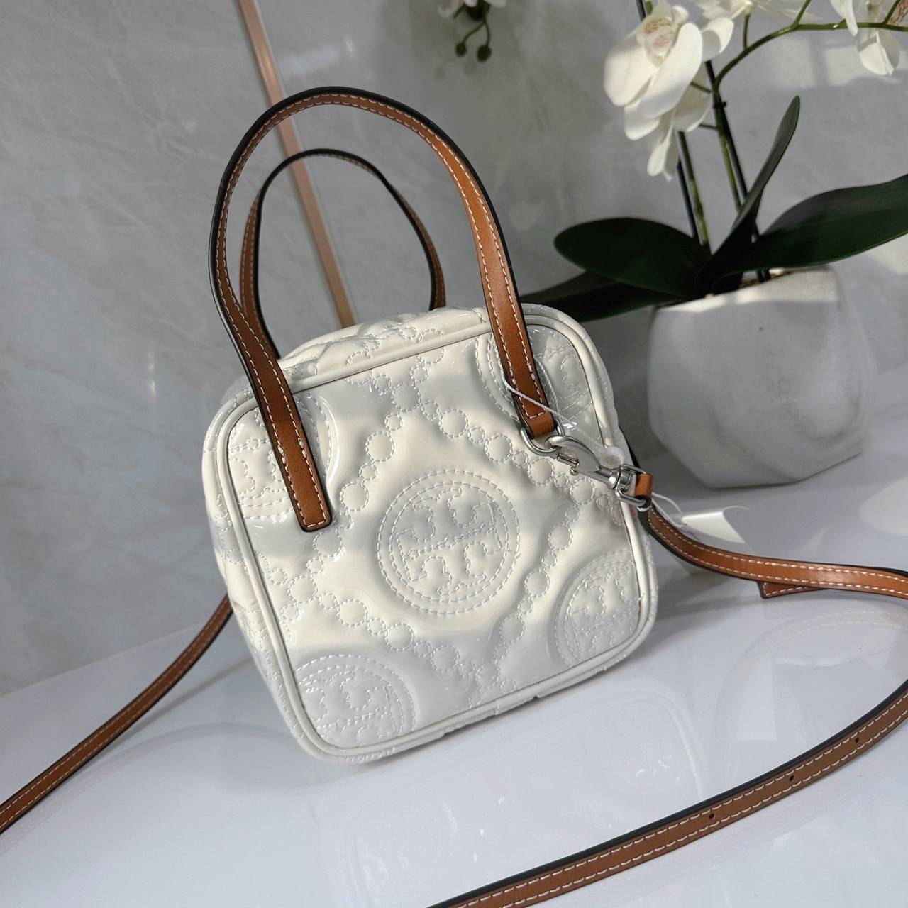 Tory Burch T Monogram Embroidered Patent Cube คอลเลคชั่นใหม่ รุ่นลิมิเต็ดรูปทรงใหม่ T Monogram สุดcube วัสดุหนังแท้ เปิด-ปิดด้วยซิป ภายในกว้าง มีช่องแยก 1 ช่อง สามารถใส่โทรศัพท์มือถือได้ทุกรุ่น สามารถถือหิ้วหรือสะพายได้ สายสามารถถอดและปรับระดับได้คะ