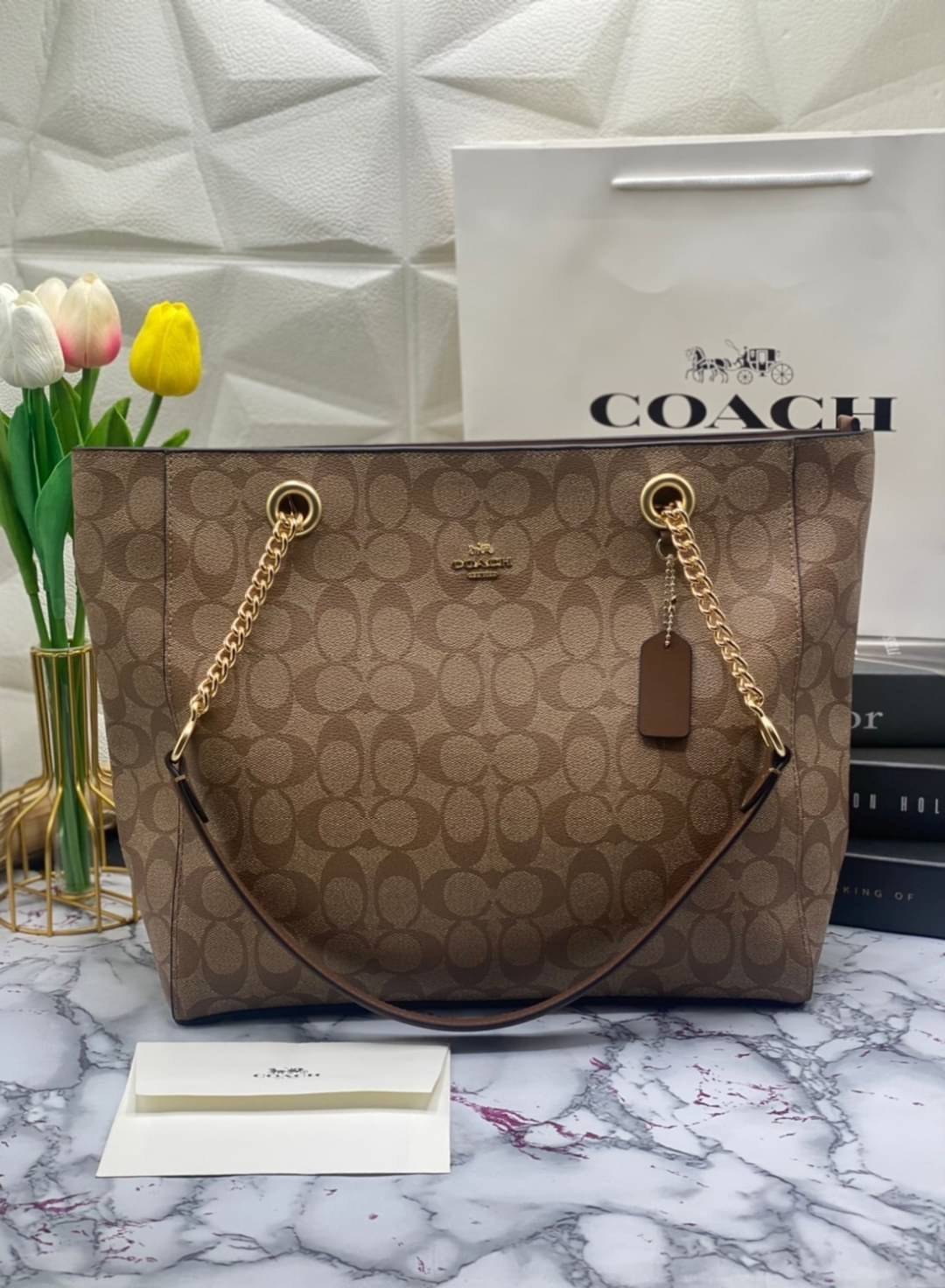COACH Tote in Signature Canvas Bag กระเป๋าสะพายทรงช้อปปิ้ง สายกระเป๋าเป็นหนังสลับโซ่ทองสวยงาม เพิ่มความหรูหรา ภายในโล่งกว้างใส่ของได้เยอะมาก วัสดุ Canvas เคลือบลายซิกเนเจอร์และหนัง พร้อมซิปกลางเก็บของได้มิดชิดเลยค่ะ มี 3 สี น้ำตาล ดำ ขาว