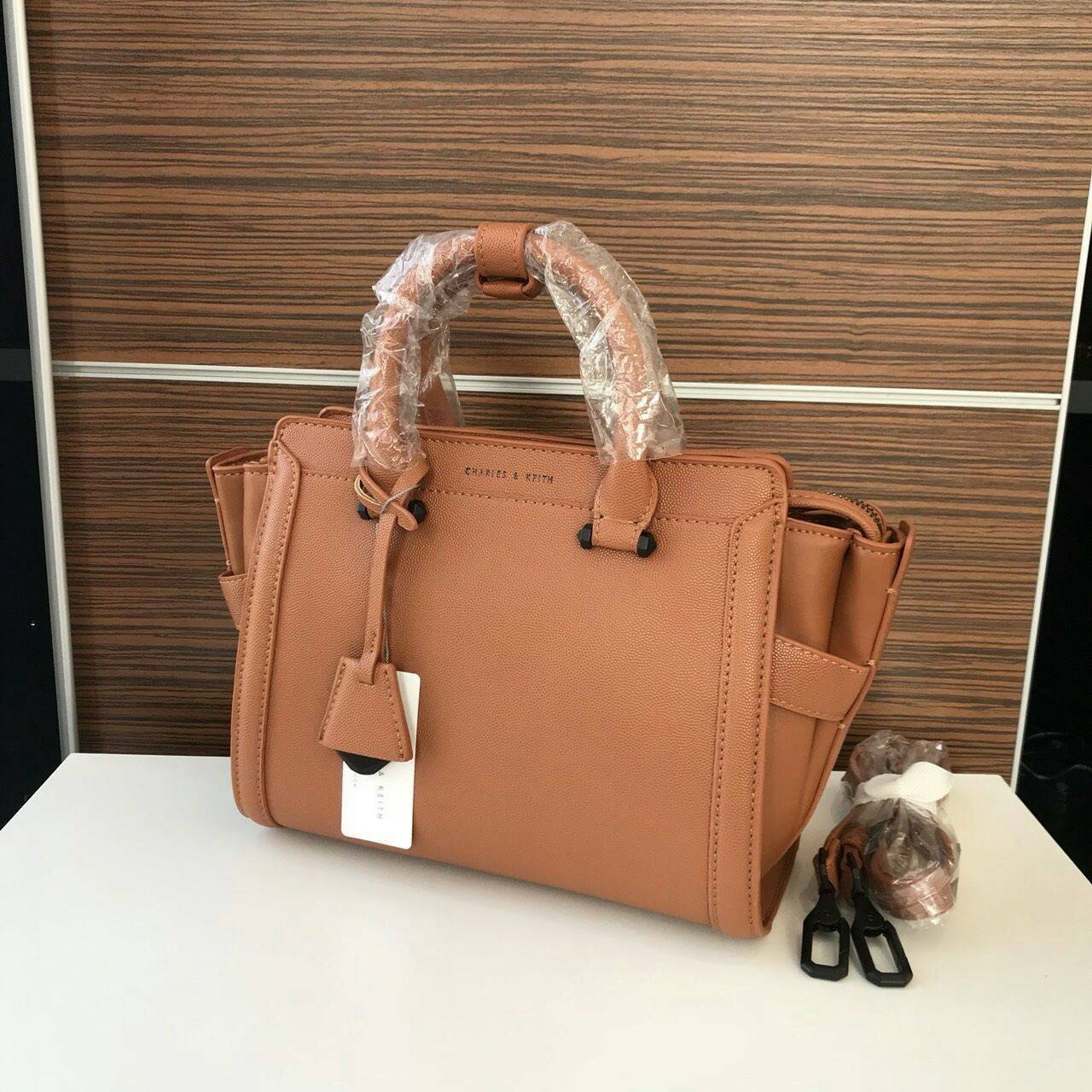CHARLES & KEITH TRAPEZE BAG Best sellwr ! กระเป๋าถือหรือสะพายรุ่นยอดนิยมดีไซน์สวยหรูวัสดุหนัง คาเวียร์อยู่ทรง ด้านข้างเเต่งหนังช่องตัดดูมีดีเทล ด้านหน้าสกรีนโลโก้ ด้านหลังมีช่องซิป เปิดปิดด้วยซิปหัวซิป ปัํ๊มโลโก้ หูจับเเข็งแรง พับลงได้ พร้อมสายสะพายหนังปร