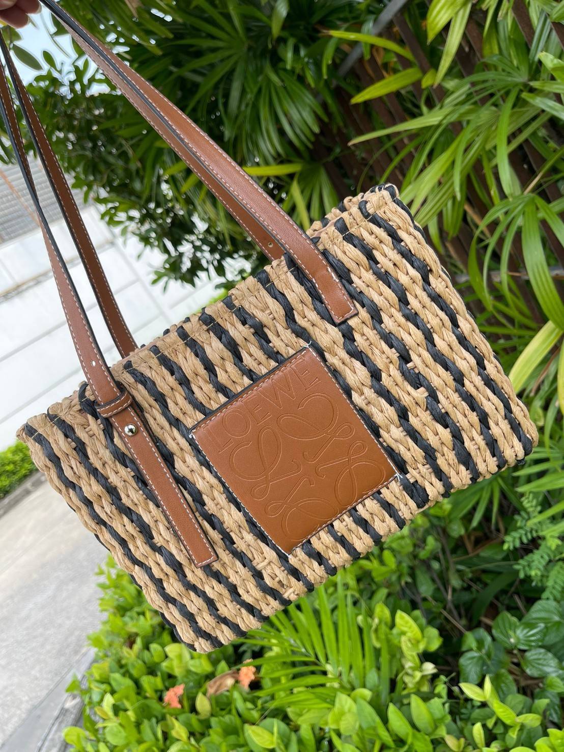 LOEWE X PAULA'S IBIZA SMALL SQUARE BASKET BAG กระเป๋าสะพายไหล่จากโลเอเว่ เป็นกระเป๋าสานขึ้นจากใบกก (Reed) ที่มีทั้งความเหนียวและความยืดหยุ่น สวยน่ารักแบบมินิมอล มีความทนทานสูง ดูแลรักษาง่าย ด้านหน้าและหูเป็นหนังแท้(calf skin) ส่วนภายในมีถุงผ้าแบบหูรู