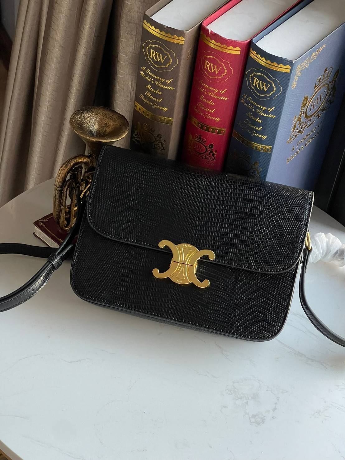 Celine MEDIUM TRIOMPHE BAG IN SHINY By croc มีรูปทรงเป็นกล่องคล้ายกับกระเป๋า Classic Box แต่มีการออกแบบโลโก้ที่สะดุดตาแบบวินเทจ ด้วยดีไซน์หรูหราและที่ดูโฉบเฉี่ยวเ้วยลงดลายcroc มีความคลาสสิคอย่างเต็มเปี่ยม ทำให้เป็นที่ดึงดูดความสนใจของสาวๆ ด้วยความคล่องตัว