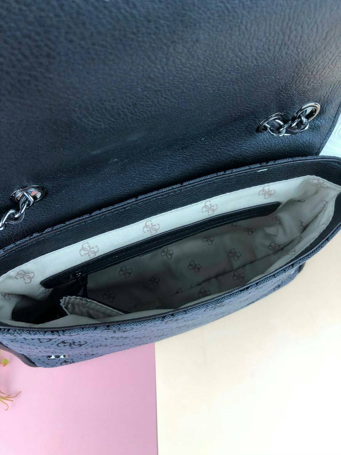 Guess Logo city handbag กระเป๋าสะพายไหล่ ตัวกระเป๋าเป็นผ้าลาย signature ของแบรนด์ ตัดกับหนังที่ตัวขอบกระเป๋า มาพร้อมพวงกุญแจโลโก้แบรนด์ ด้านหน้ามีโลโก้แบรนด์ ด้านหลังมีช่องใส่โทรศัพท์/บัตรได้ เปิดปิดแบบกระดุมแม่เหล็กซ้าย-ขวา ด้านในมีช่องซิป เล็ก 1 ช่อง แล