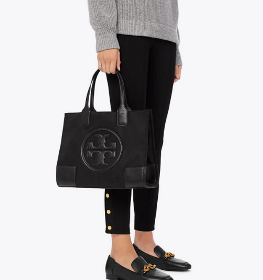 กระเป๋าทรงโท้ทใบใหญ่ TORY BURCH ELLA TOTE BAG วัสดุ NYLON ทั้งใบตัดด้วยหนังสีดำ แต่งโลโก้แบรนด์ด้านหน้า ด้านข้างมีกระดุม สามารถขยายทรงได้ ด้านในเปิดปิดด้วยกระดุมแม่เหล็กฝัง ช่องกว้างหลักหนึ่งช่องและช่องซิปอีกช่อง สามารถใส่แล็ปท็อปได้สบาย ใบใหญ่เว่อวัง ไอเ
