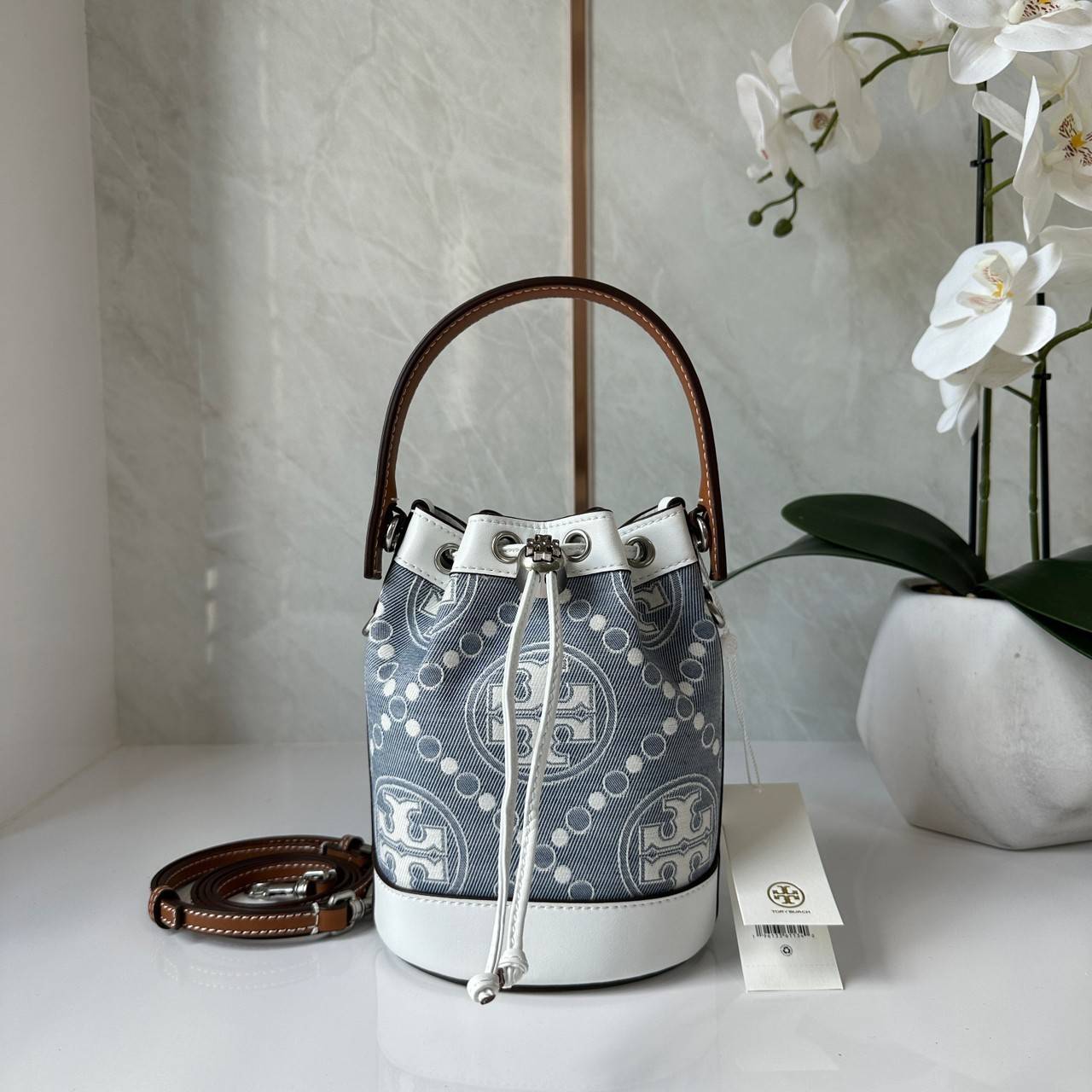 TORY BURCH Mini T Monogram Denim Bucket Bag คอลเลคชั่นใหม่ รูปแบบคลาสสิค พกพาความหรูหราไปได้ทุกที่ด้วยกระเป๋าทรง Bucket ขนาดกลางและปิดด้วยเชือกรูดพร้อมโลโก้แวววาว วัสดุผ้าเดนิมแจ็คการ์ด ตัดขอบหนังแท้ สวยหรู ทันสมัยสุดๆคะ