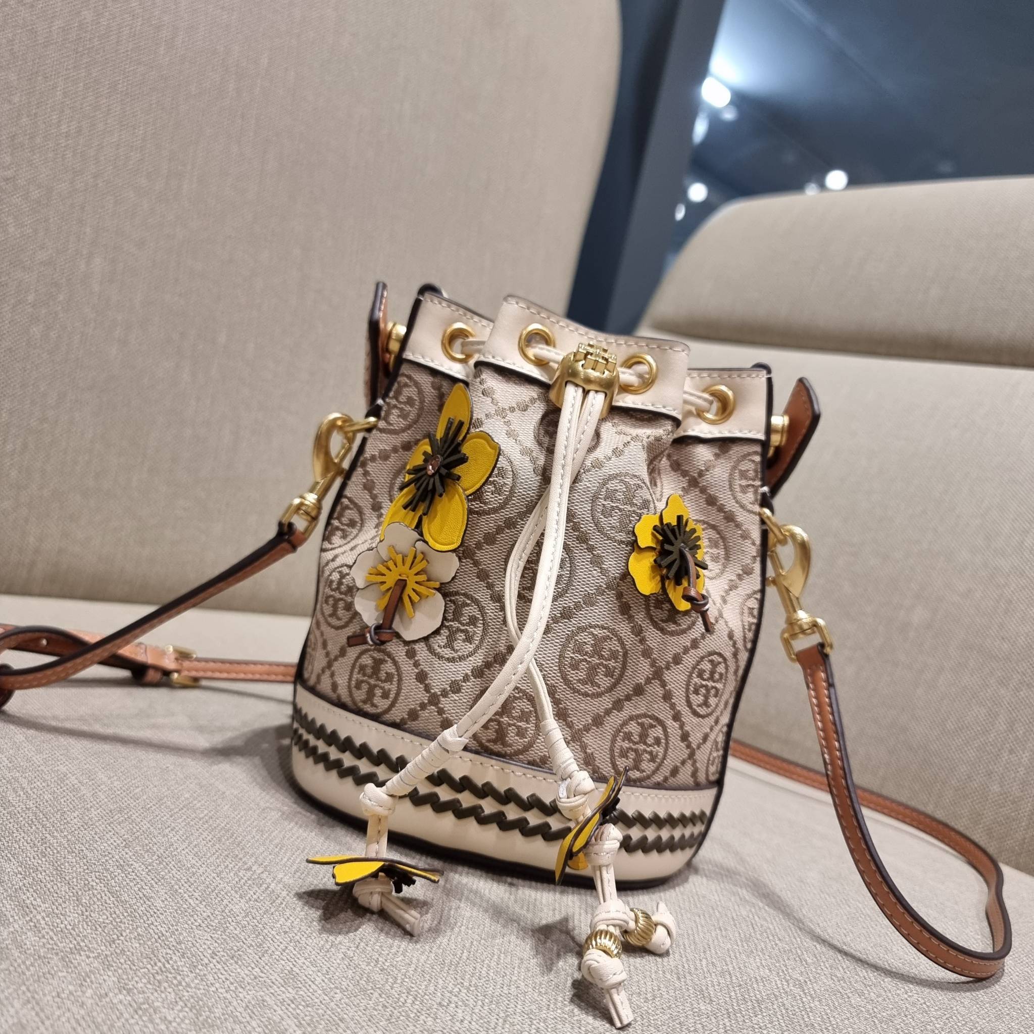 TORY BURCH MINI T MONOGRAM FLORAL BUCKET BAG คอลเลคชั่นใหม่ พร้อมเสิร์ฟความสวยให้ถึงบ้าน!! กระเป๋าบัคเก็ตทรงยอดนิยม ไซส์มินิ ดีไซน์ใหม่ล่าสุด สไตล์งานคราฟ มีลูกเล่นประดับดอกไม้กับตัวกระเป๋า และตัวรูดสาย วัสดุผ้า jacquard ตัดสลับหนังแท้ หูจับและขอบกระเป๋าต