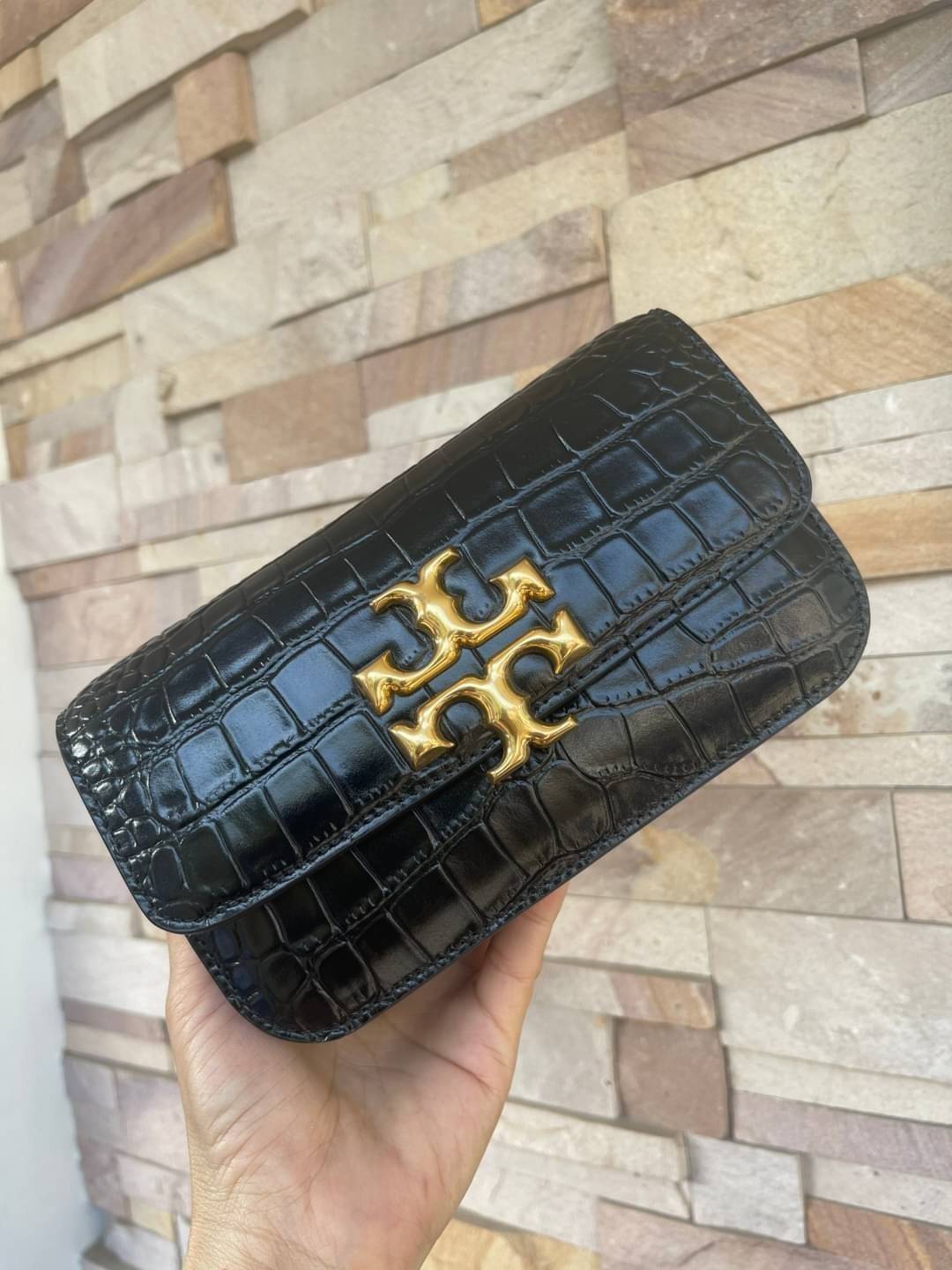 Tory Burch Eleanor Crocodile-Embossed Phone Crossbody Bag จุดเด่นของรุ่นนี้คือดีไซน์ออกมาในสไตล์คลาสสิกที่มาพร้อมกับฮาร์ดแวร์ที่ทำจากวัสดุทองเหลืองและสายสะพายโซ่เกลียวสีทอง ซึ่งการออกแบบได้รับแรงบันดาลใจมาจากเครื่องประดับ รูปทรงกะทัดรัดจึงสามารถสะพายใช้งา