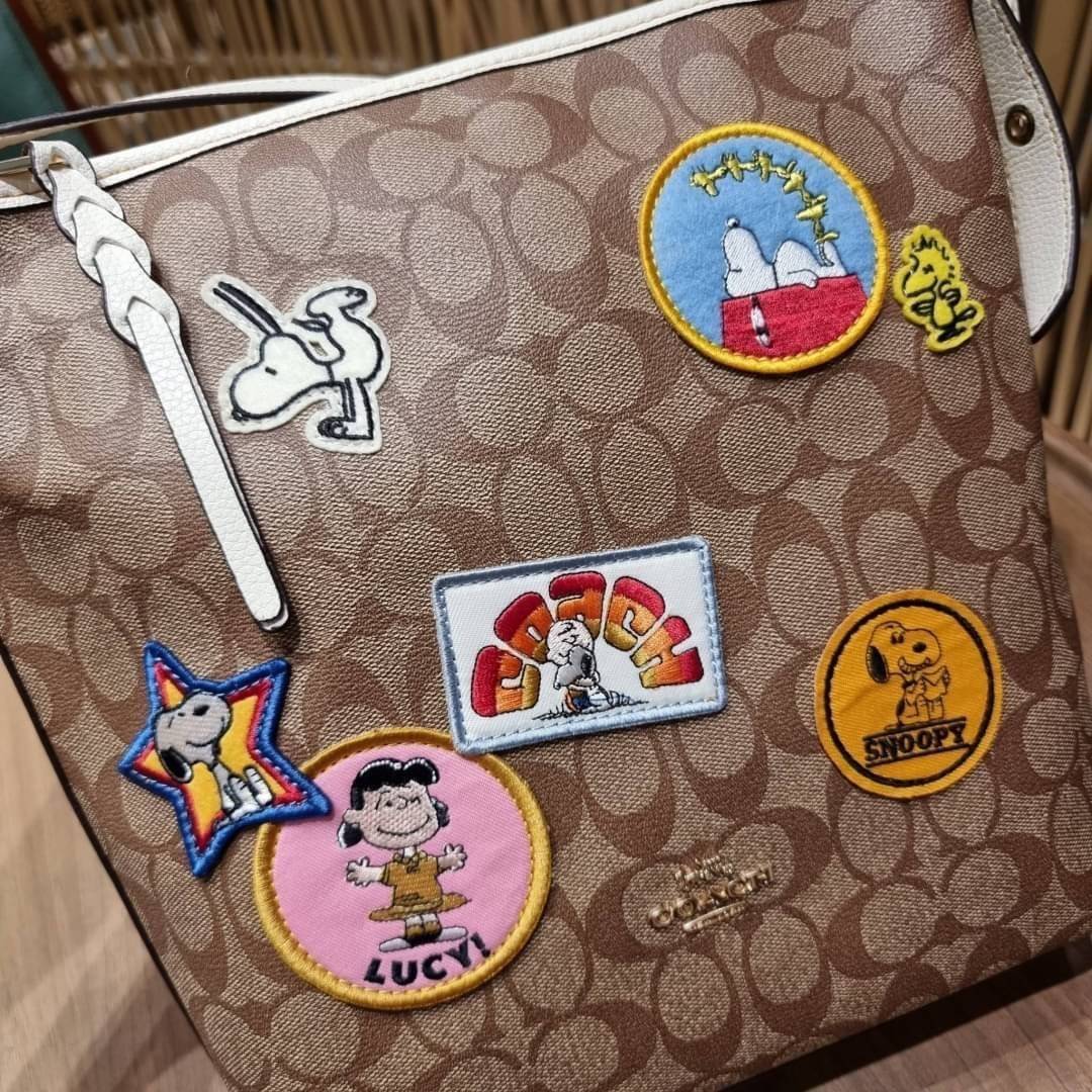 OUTLET 】COACH C4112 COACHxPEANUTS VAL DUFFLE IN SIGNATURE CANVAS WITH VARSITY PATCHES ใหม่ล่าสุด กระเป๋าทรงดัฟเฟิล ที่มาพร้อมเหล่าผองเพื่อนสนูปพี สวยมีเอกลักษณ์ ทรงกระเป๋าไม่ซ้ำใคร แถมยังใส่ของได้จุใจไปอีก วัสดุหนังแคนวาสคุณภาพดี ด้านหลังมีช่องซิป กระเป๋า