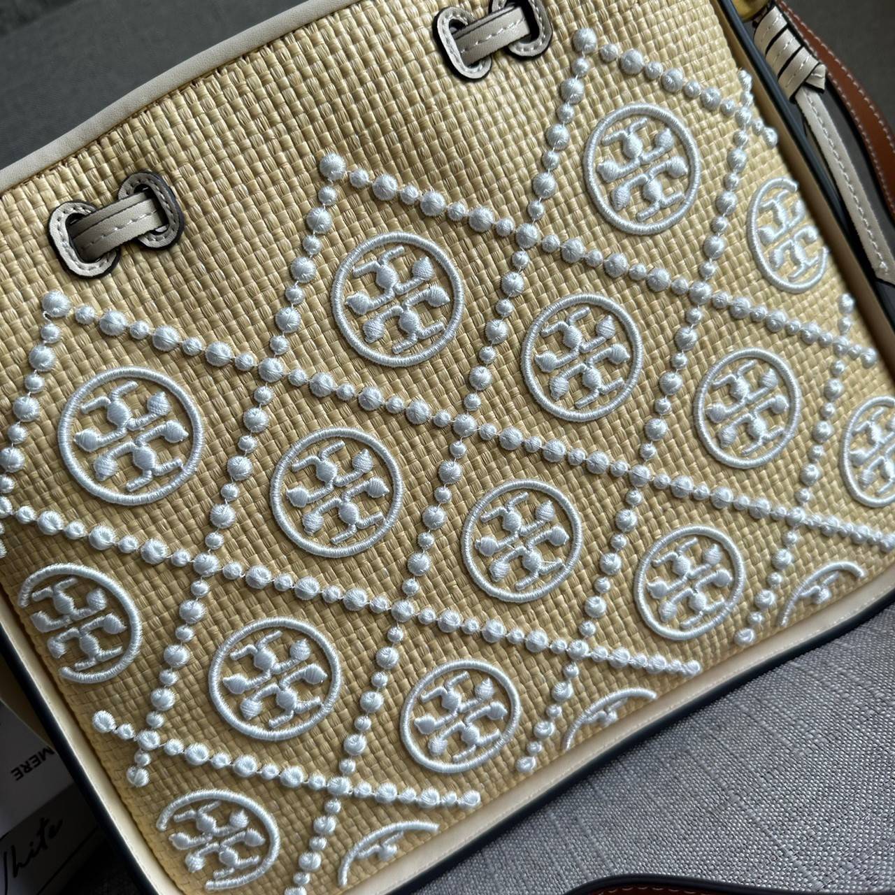 TORY BURCH T Monogram Straw Bell Bag กระเป๋าสะพายข้างรุ่นคลาสสิกที่ได้แรงบันดาลใจจากการควิลท์แบบดั้งเดิมของเพนซิลเวเนีย คอลเลกชันบ่งบอกถึงความมีสไตล์เหนือกาลเวลา รูปทรงเรียวโดดเด่น ปักทอลายแบรนด์อย่างสวยงาม เปิด ปิดด้วยเชือกรูด ด้านในช่องโล่งกว้าง ซับในผ้