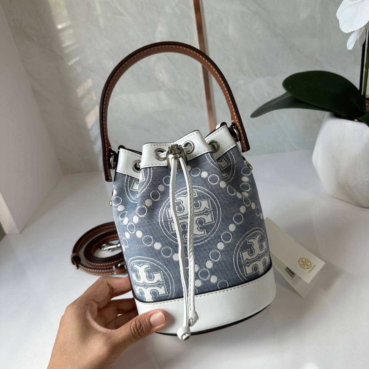 TORY BURCH Mini T Monogram Denim Bucket Bag คอลเลคชั่นใหม่ รูปแบบคลาสสิค พกพาความหรูหราไปได้ทุกที่ด้วยกระเป๋าทรง Bucket ขนาดกลางและปิดด้วยเชือกรูดพร้อมโลโก้แวววาว วัสดุผ้าเดนิมแจ็คการ์ด ตัดขอบหนังแท้ สวยหรู ทันสมัยสุดๆคะ