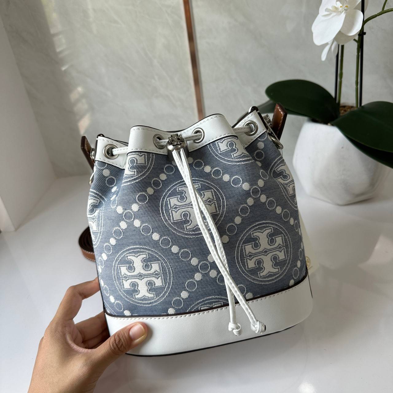 TORY BURCH T Monogram Denim Bucket Bag MEDIUM คอลเลคชั่นใหม่ รูปแบบคลาสสิค พกพาความหรูหราไปได้ทุกที่ด้วยกระเป๋าทรง Bucket ขนาดกลางและปิดด้วยเชือกรูดพร้อมโลโก้แวววาว วัสดุผ้าเดนิมแจ็คการ์ด ตัดขอบหนังแท้