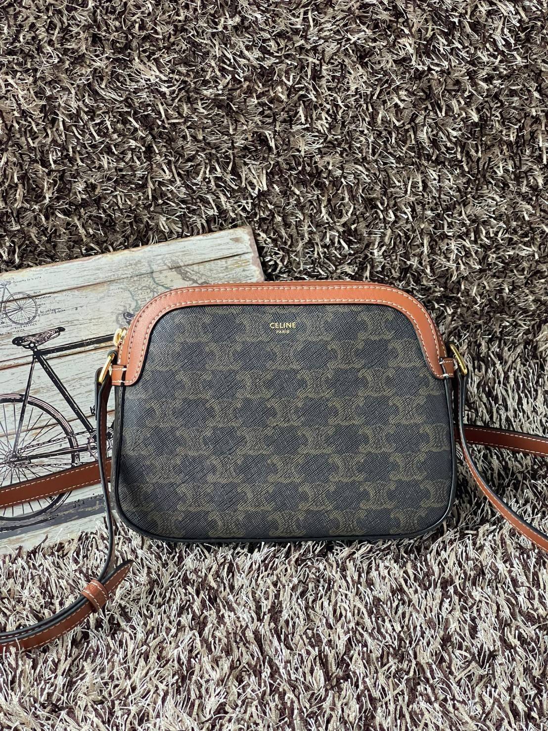 CELINE Triomphe Canvas Small Camera กระเป๋าสะพายไหล่สุดเก๋ใบนี้ผลิตจากผ้าใบเคลือบอย่างดีพร้อมขอบหนังสีน้ำตาล มาพร้อมสายสะพายหนังปรับระดับได้พร้อมฮาร์ดแวร์สีทองและซิปด้านบน ภายในบุด้วยผ้าสีน้ำตาล ลวดลาย triomphe อันเป็นเอกลักษณ์ของแบรนด์ และเป็นกระเป๋าสะพา