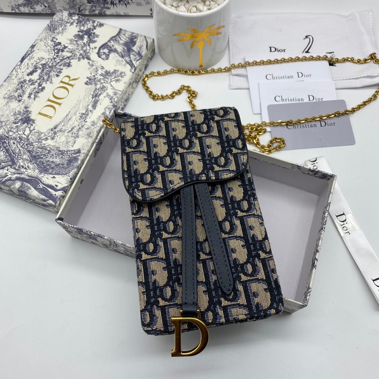 หนังแท้ DIOR PHONE BAG / DIOR PHONE HOLDER BAG กระเป๋าใส่โทรศัพท์เอกลักษณ์ของความหรู สายสะพายโซ่อะไหล่ทอง วัสดุหนังแท้และผ้า Jacquard อย่างดีสวยงามที่สุด ผสมผสานความสง่างามและคลาสสิกที่เข้ากับยุคสมัย ด้านหน้าโดดเด่นด้วยซิกเนเจอร์แบรนด์ เป็นอีกหนึ่งรุ่นที่