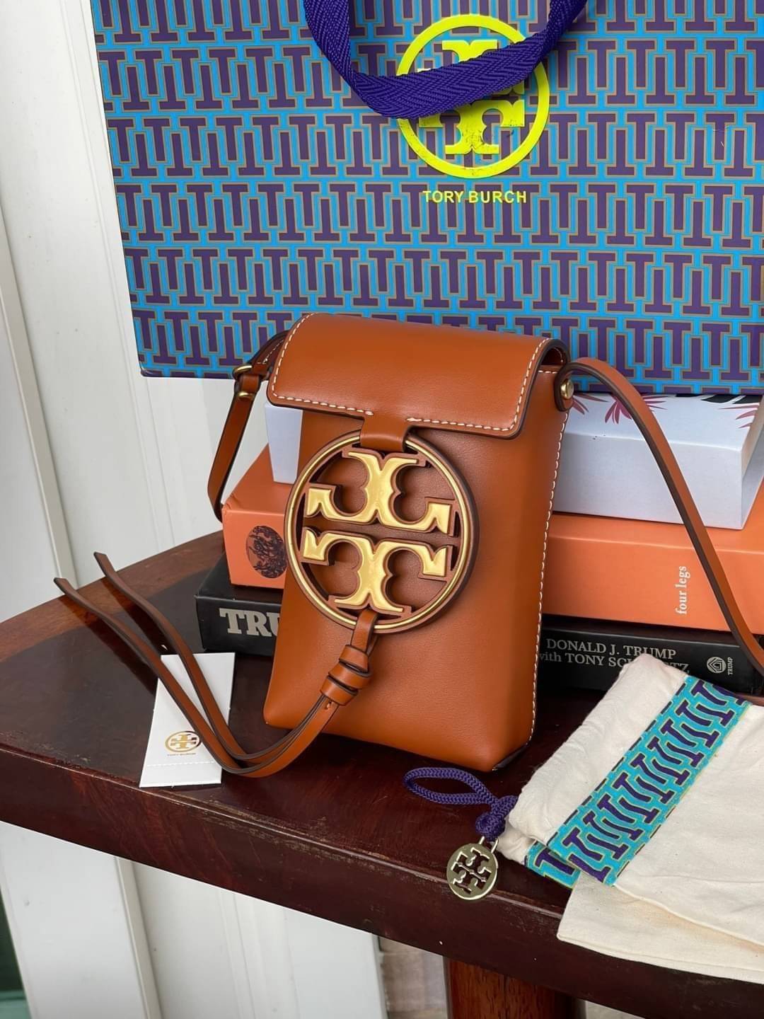 TORY BURCH MILLER METAL PHONE CROSSBODY อีกหนึ่งกระเป๋าใส่มือถือรุ่นฮิตที่เชื่อว่าหลาย ๆ คนต้องเคยเห็นผ่าน ๆ ตามาอย่างแน่นอน กับแบรนด์ Tory Burch ดีไซน์กระเป๋าทรงฝาพับแม่เหล็กใช้งานง่าย มาพร้อมดีเทล Logo แบรนด์โดดเด่นสีทองตัดกับหนังแกะสีดำ ดูหรูดูแพง! แต่