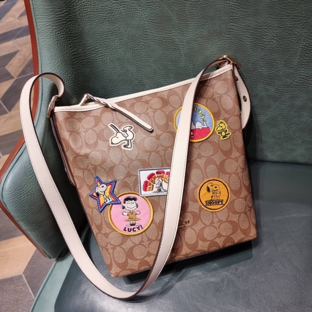 OUTLET 】COACH C4112 COACHxPEANUTS VAL DUFFLE IN SIGNATURE CANVAS WITH VARSITY PATCHES ใหม่ล่าสุด กระเป๋าทรงดัฟเฟิล ที่มาพร้อมเหล่าผองเพื่อนสนูปพี สวยมีเอกลักษณ์ ทรงกระเป๋าไม่ซ้ำใคร แถมยังใส่ของได้จุใจไปอีก วัสดุหนังแคนวาสคุณภาพดี ด้านหลังมีช่องซิป กระเป๋า