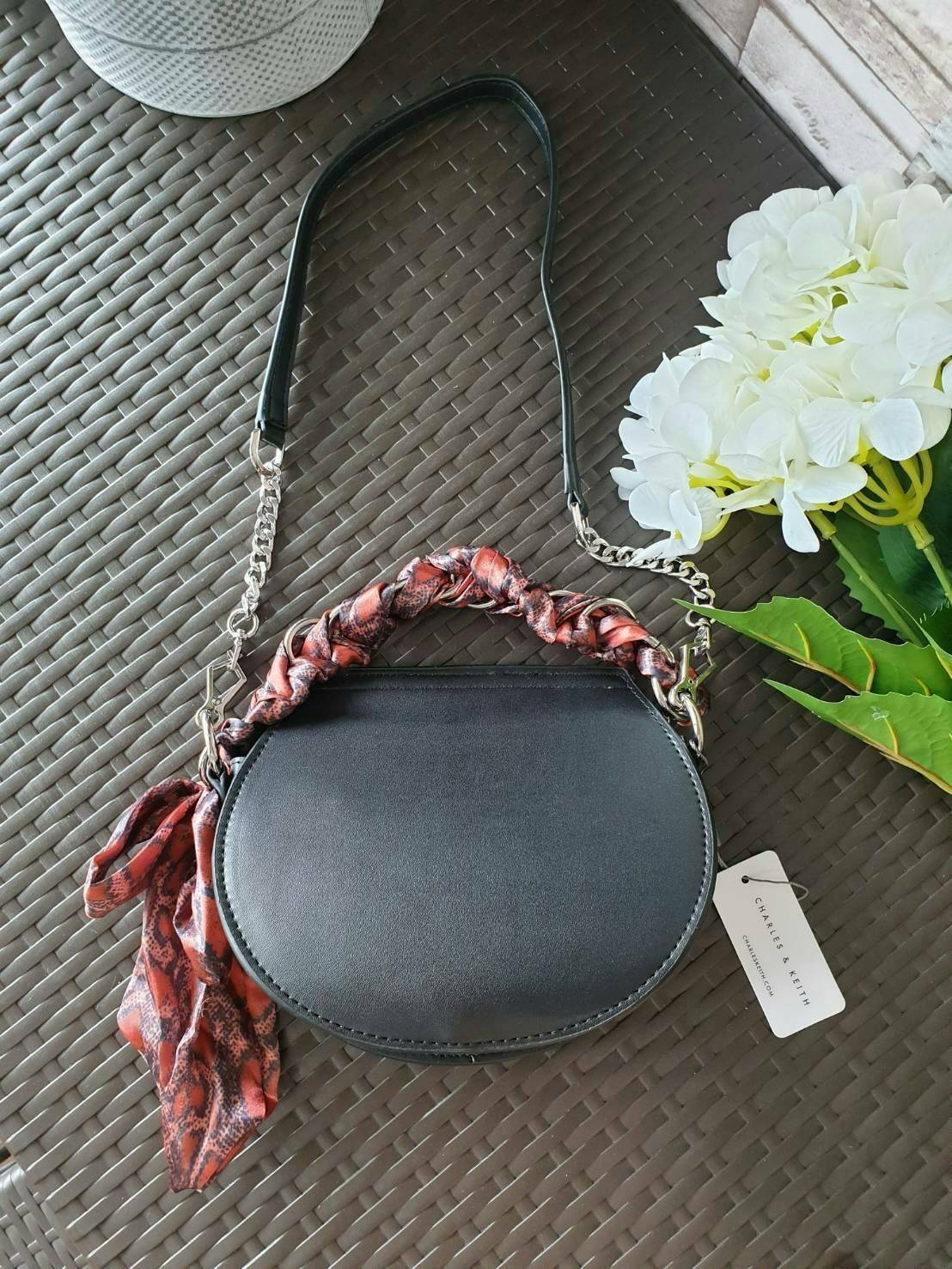 CHARLES & KEITH รุ่น LEATHER SATIN SCARF CROSSBODY BAG SL2-50150828 ราคาปกติช้อป ( ฿3,590.00 ) กระเป๋าถือ และ สะพาย ทรงโค้งมน หนังเรียบ ตั้งอยู่ทรง ด้านหน้าติดโลโก้แบรนด์ อะไหล่เงิน หูจับสายกระเป๋าร้อยเข้ากับห่วงเหล็กกลมๆ ด้วยผ้าลายสวยงามผูกเป็นโบว์เก๋ๆ ถ